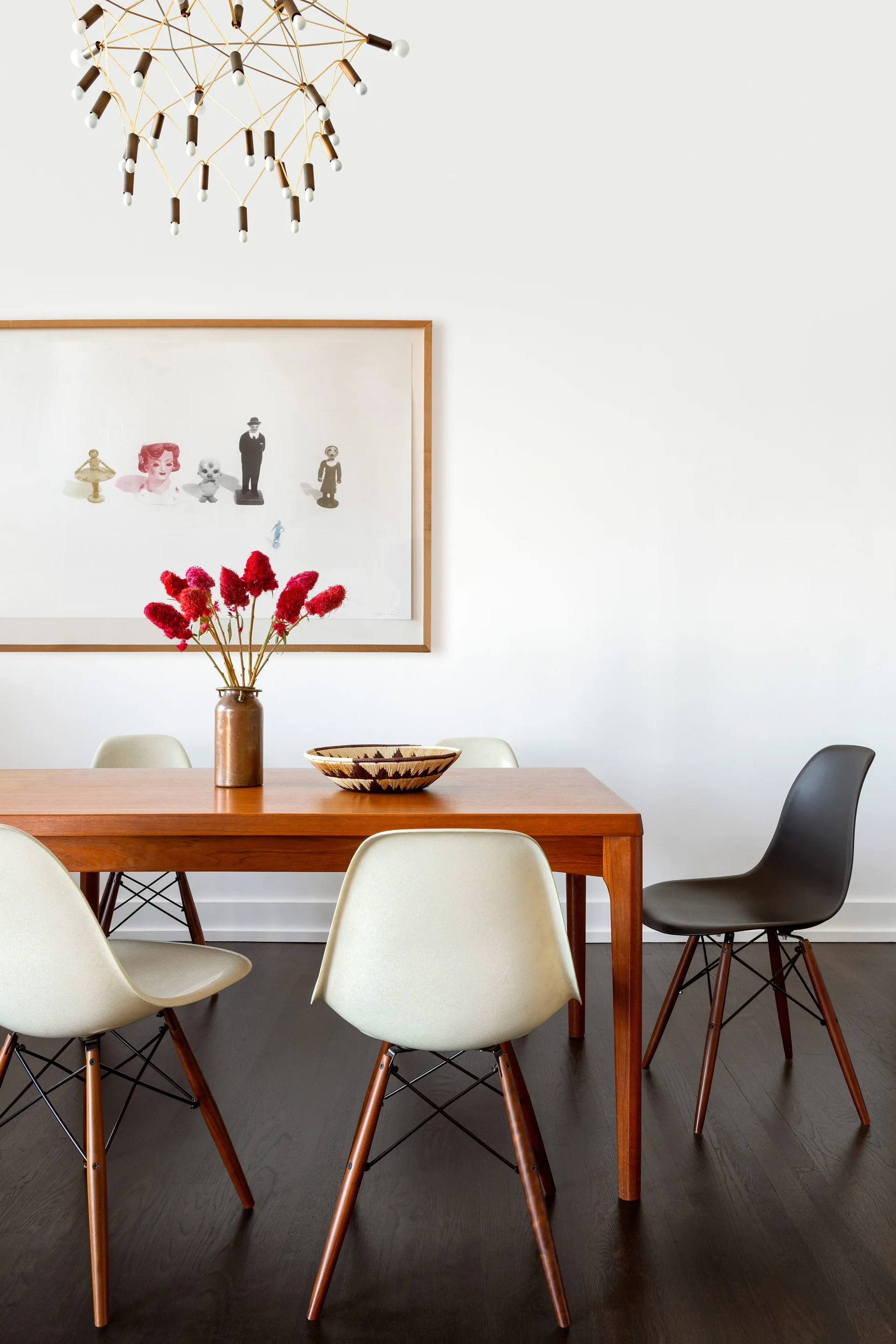 A wooden dining table with cream and black molded shell chairs sits under a branching gold chandelier on dark wood flooring.