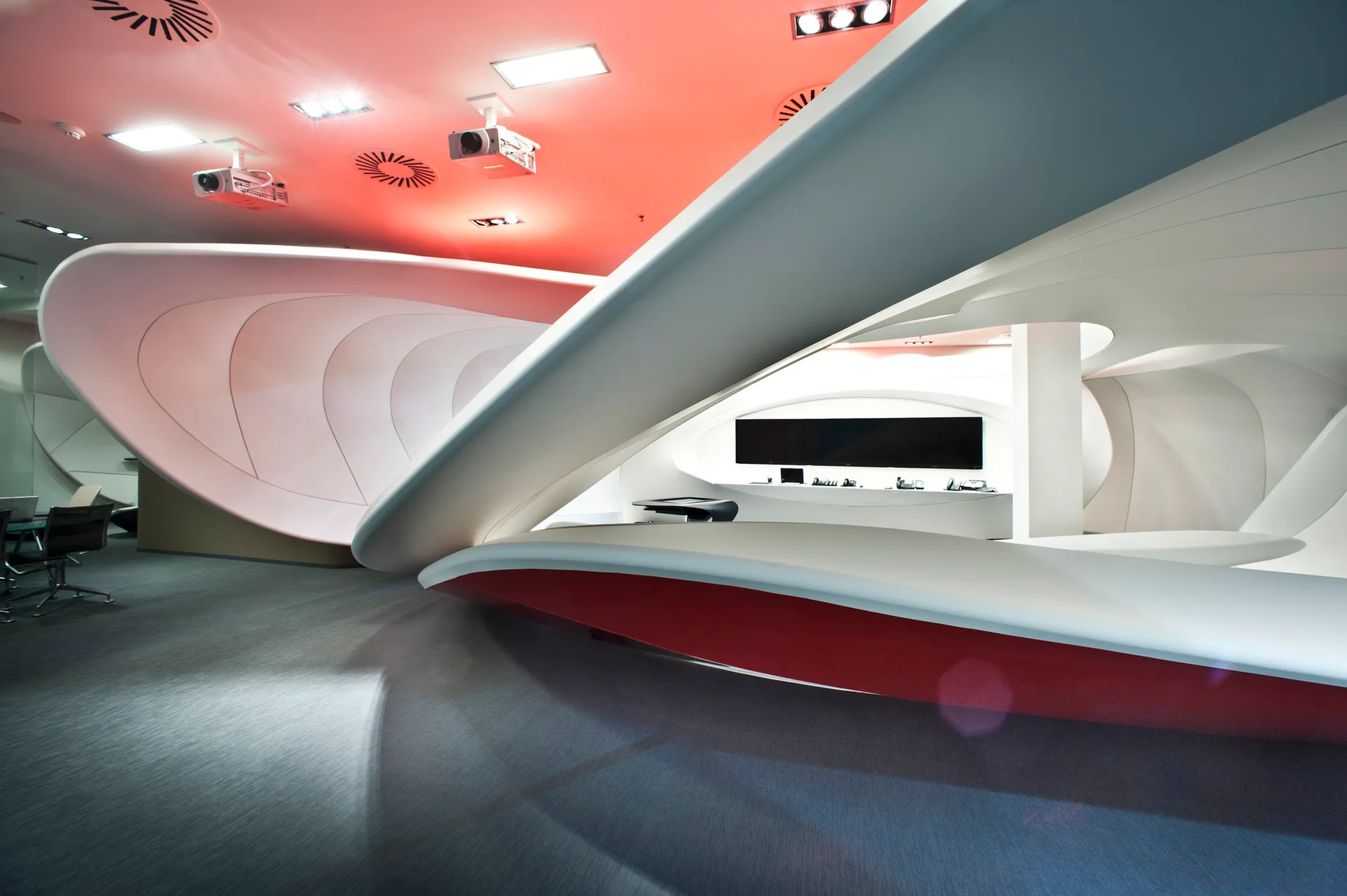 A futuristic corporate space with sculptural curved white partitions, a modern reception desk with a red underside, and red ceiling lighting.