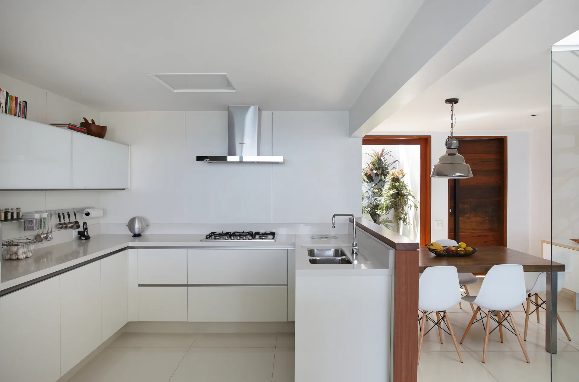 Modern white kitchen with flat-panel cabinets, a stainless steel hood, and a wooden half-wall separating the counter from an adjacent dining table.