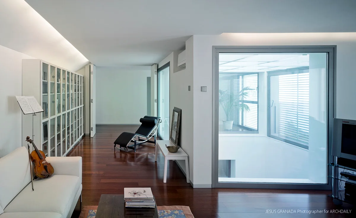 A minimalist living room with a white sofa, dark wood floors, and glass-fronted bookcases opposite a large window overlooking a light well.