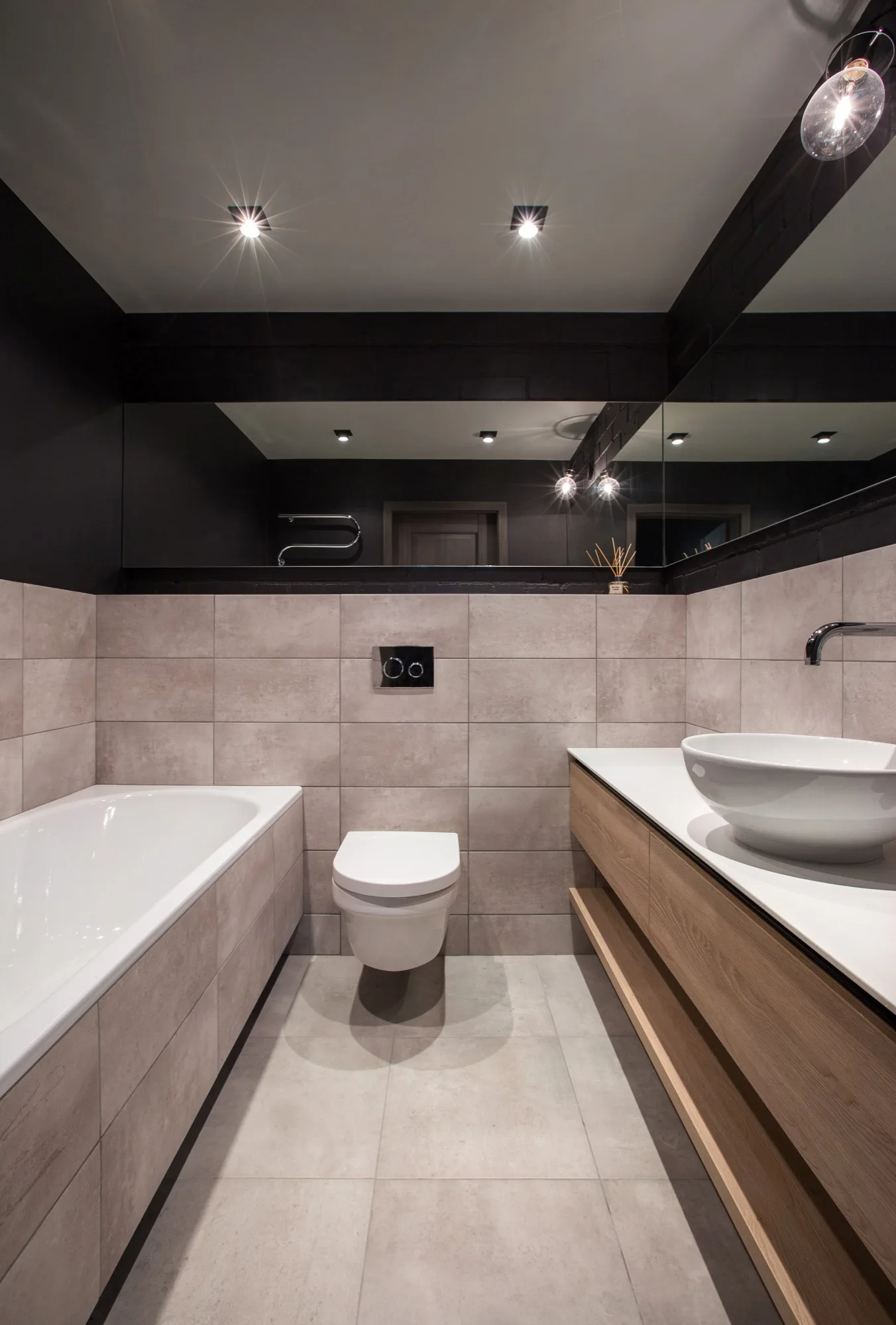 A modern bathroom with a floating wooden vanity, a vessel sink, a wall-mounted toilet, and large-format beige wall tiles.