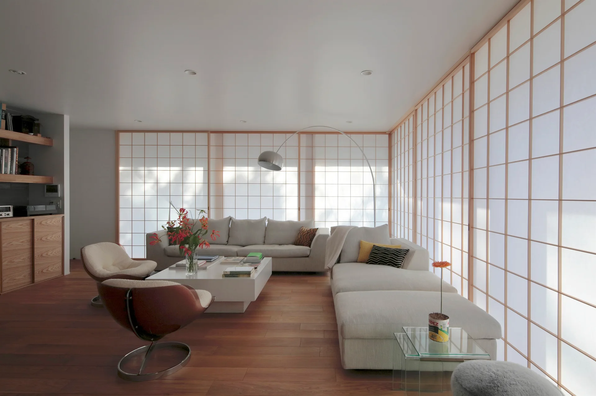 A minimalist living room featuring a modular cream sofa, two swivel armchairs, a low white coffee table, and a wall of paper shoji screens.