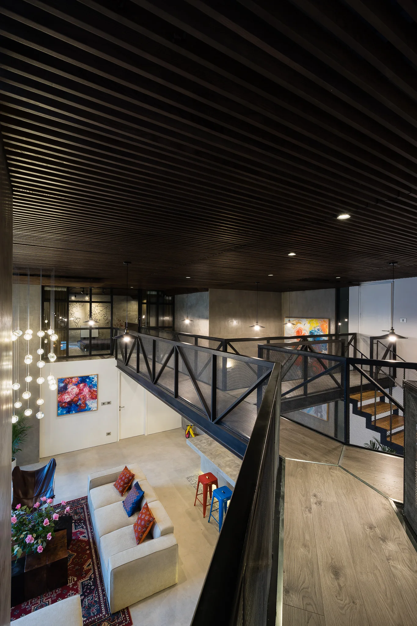 An industrial double-height living room features a mezzanine walkway with black mesh railings beneath a dark slatted wood ceiling.