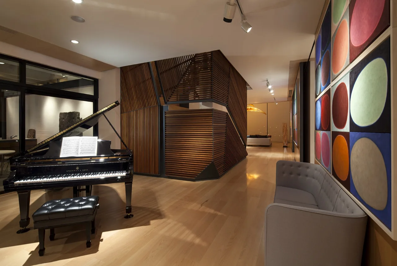 A modern living area features a black grand piano, a grey tufted sofa, colorful circular grid wall art, and an angular slatted wood room divider.