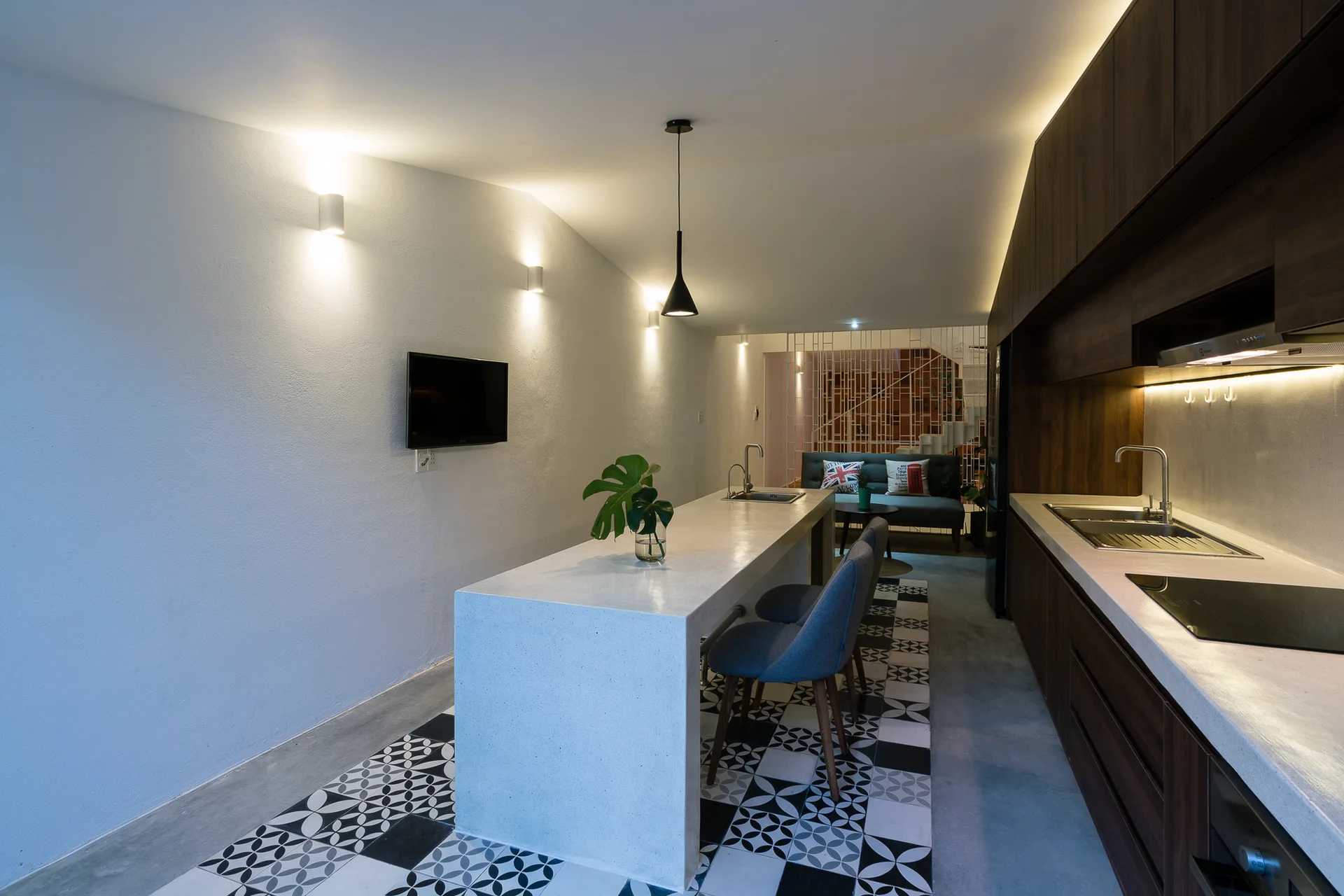 A contemporary kitchen featuring a long white stone island over geometric floor tiles, dark wood cabinetry, and blue bar chairs.