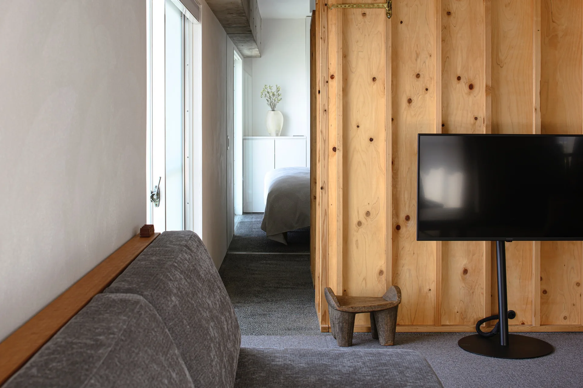A modern living room featuring a gray fabric sofa and a flat-screen television mounted next to a natural plywood room divider.