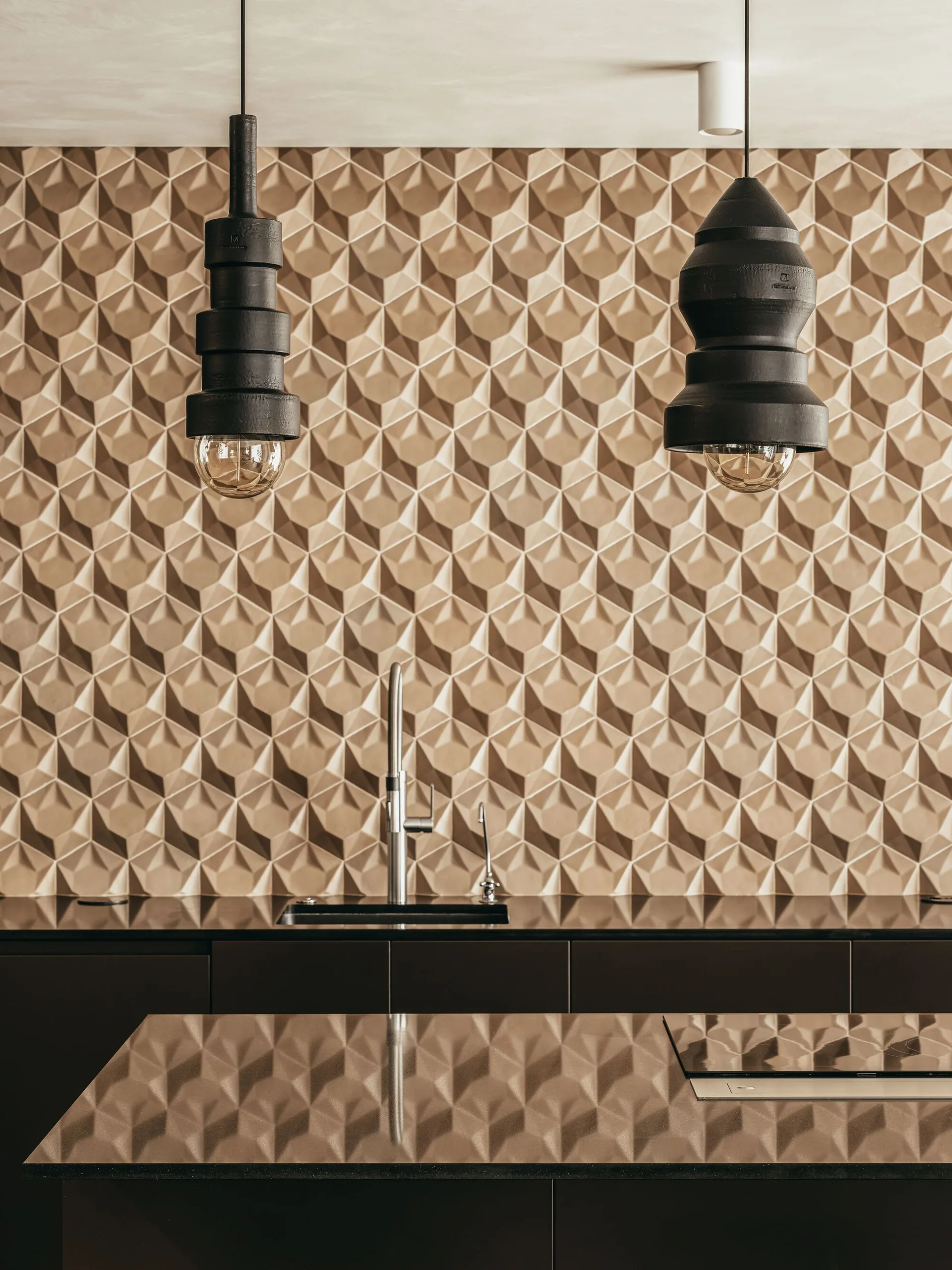 A modern kitchen with a brown geometric 3D tile backsplash, dark countertops, a chrome faucet, and hanging black pendant lights.