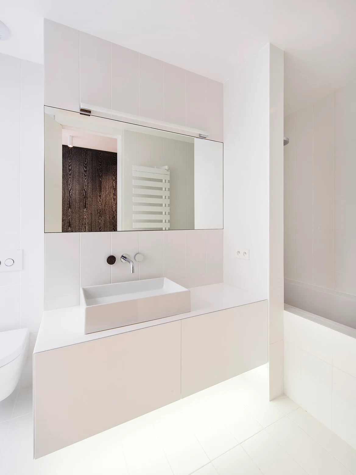 A modern white bathroom features a floating vanity cabinet with a rectangular vessel sink and a large wall-mounted mirror.