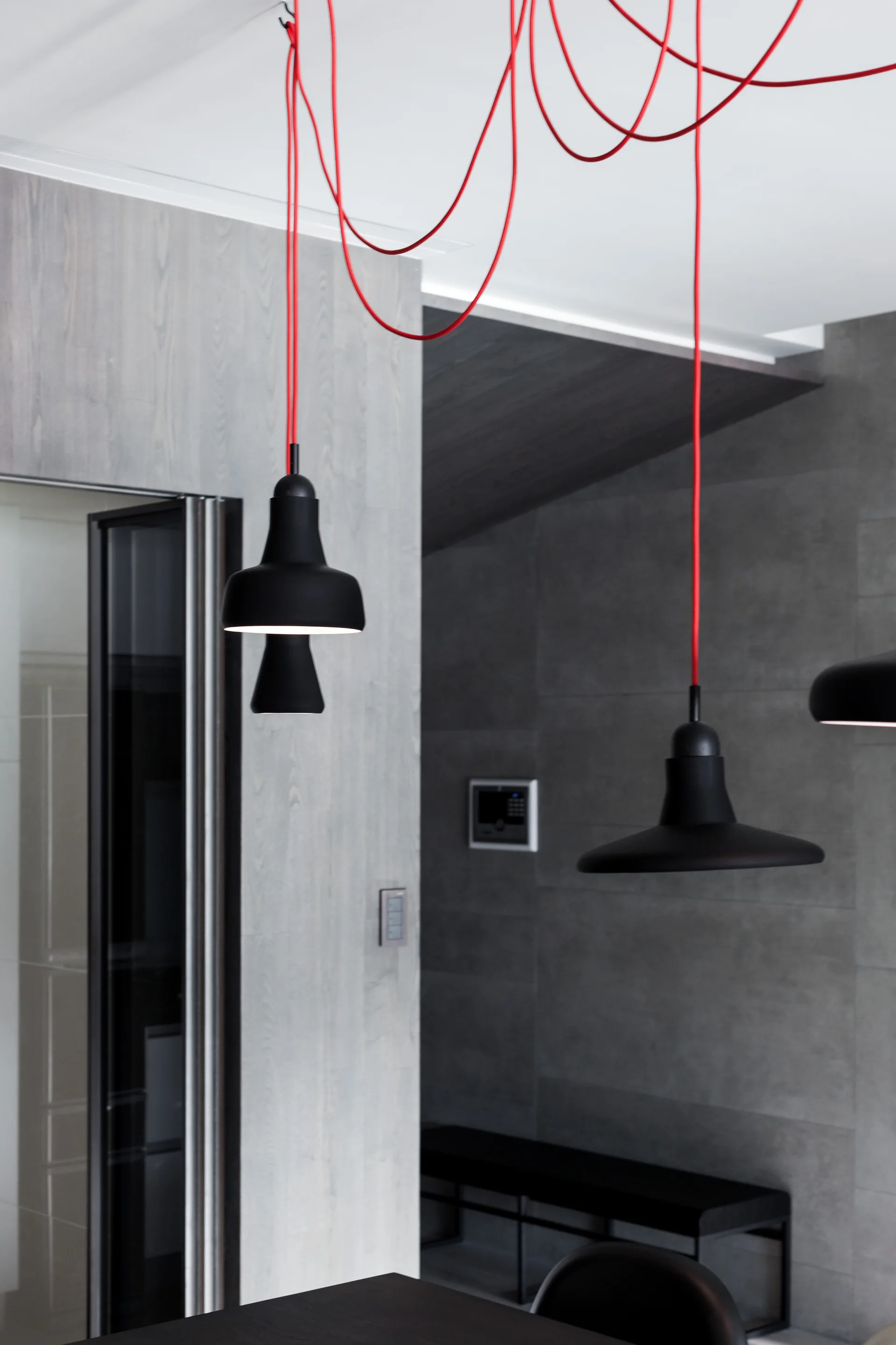 Matte black pendant lights hang from bright red cords swagged across a white ceiling against grey tiled and wood-paneled walls.