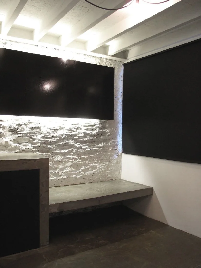 An interior space features a textured white painted brick wall, a built-in smooth concrete bench, and black wall-mounted cabinets.