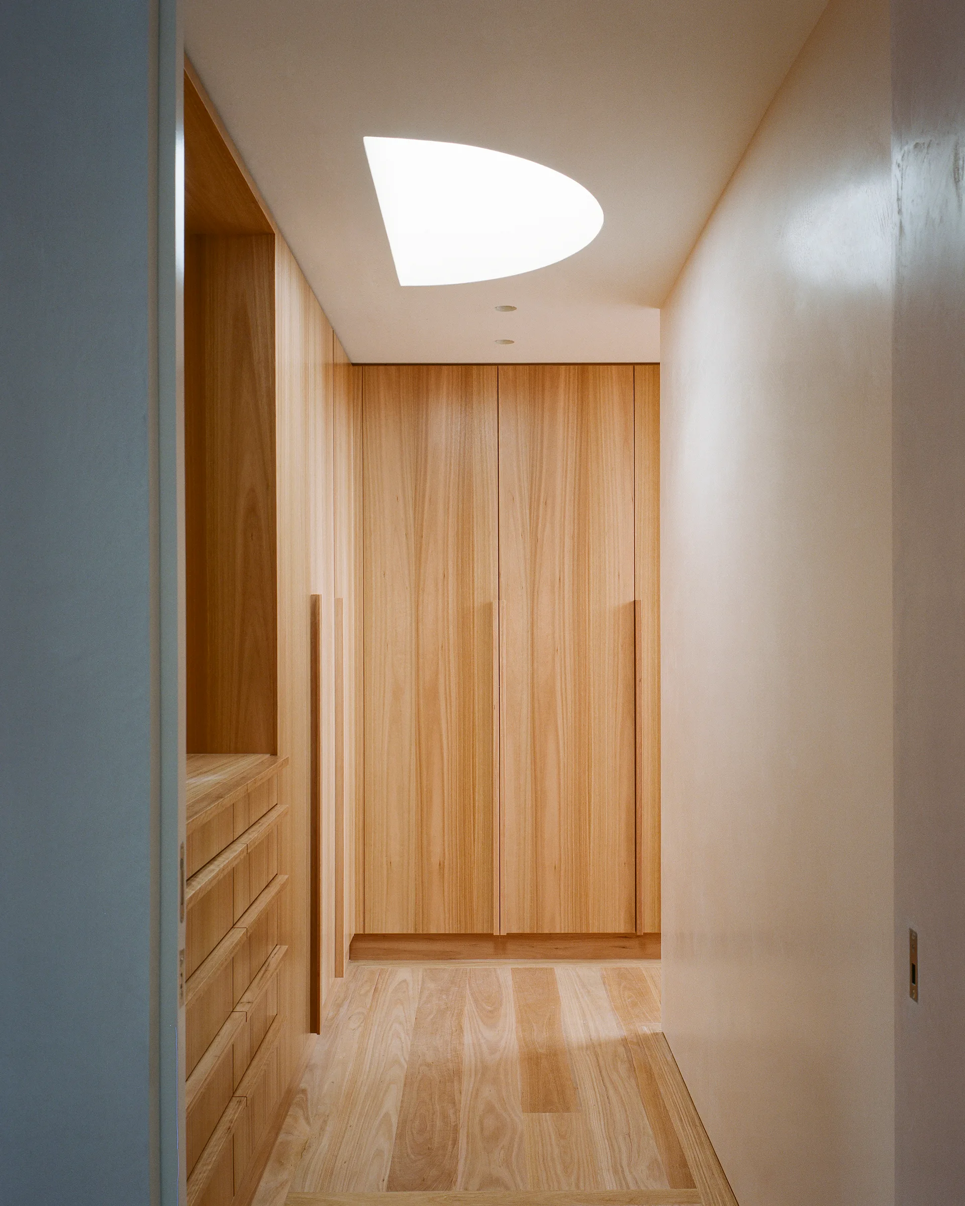 A minimalist walk-in closet features floor-to-ceiling light wood cabinetry, built-in drawers, and a unique semicircular skylight overhead.