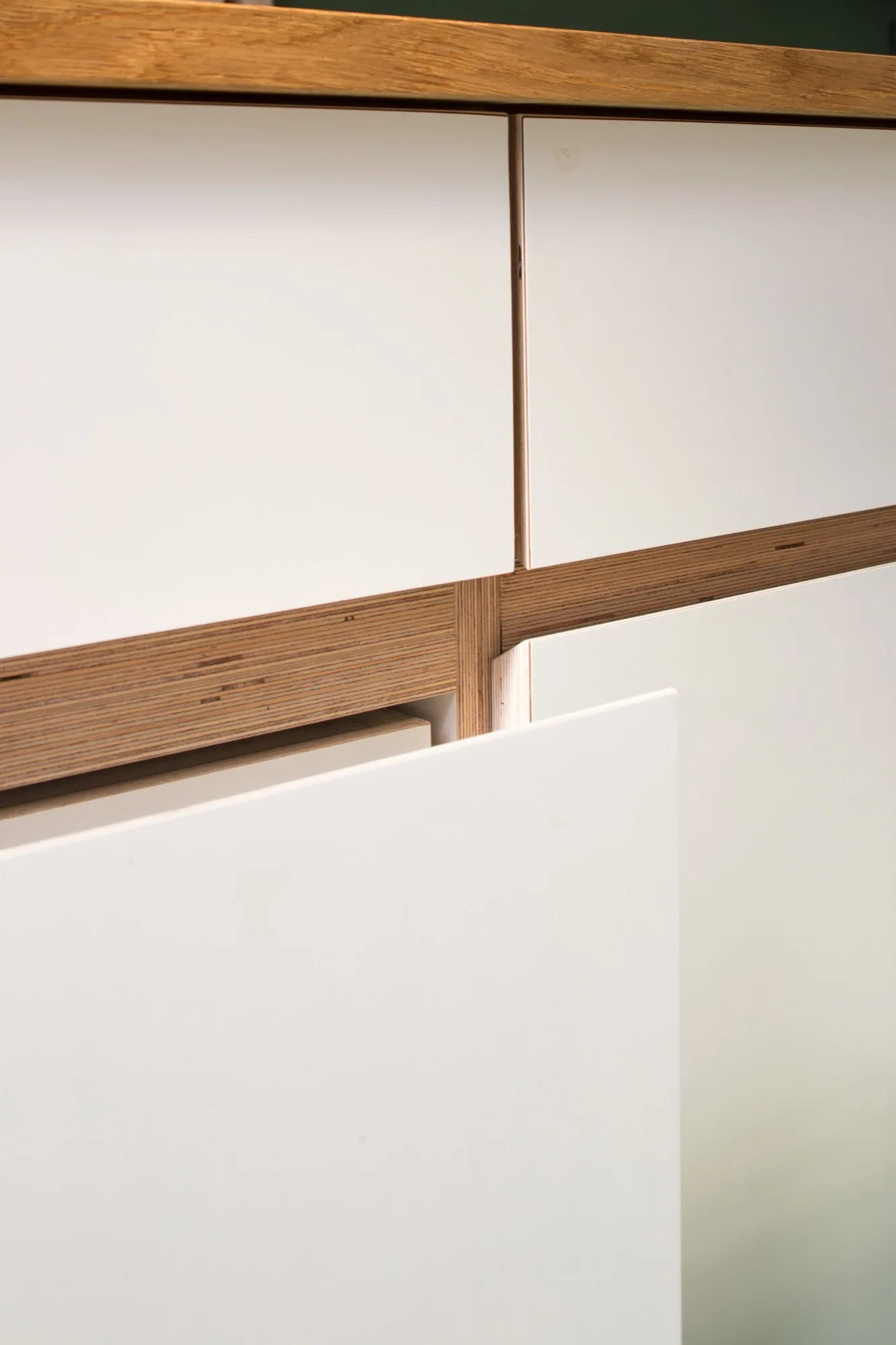 A close-up view of flat-front white kitchen cabinets showing exposed multi-layered plywood edges and a light wood countertop.