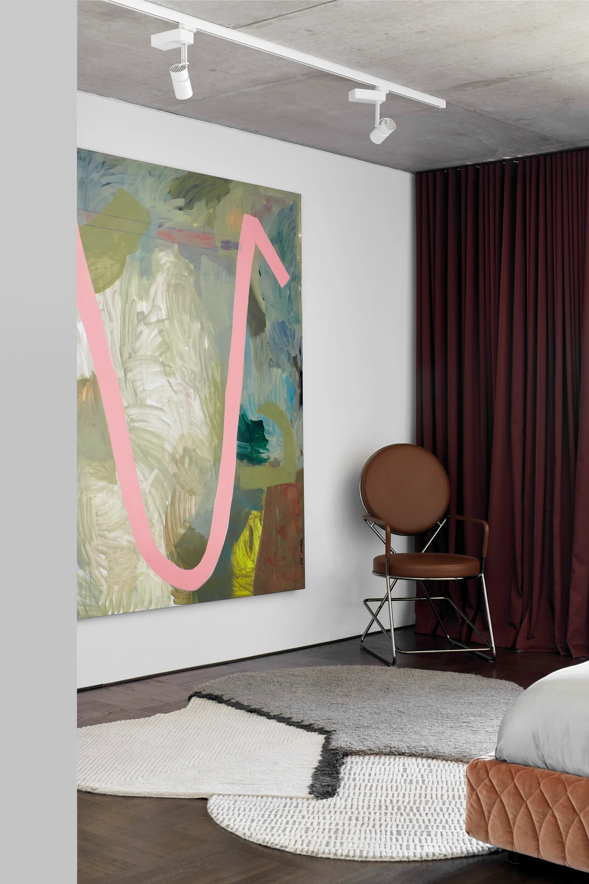 A bedroom corner featuring a circular leather accent chair, deep maroon curtains, layered rugs, and a large abstract painting on the wall.