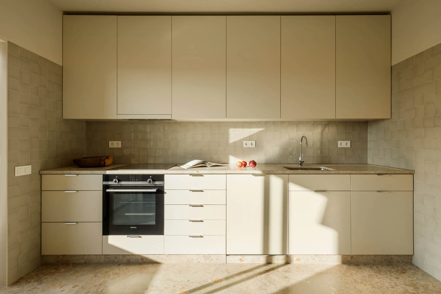 A minimalist kitchen featuring cream flat-panel cabinetry, a matching square tile backsplash, and a built-in oven.