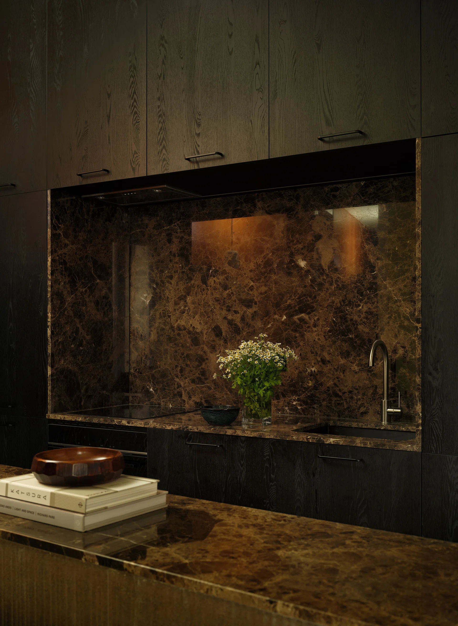 A dark wood kitchen cabinet wall featuring a recessed niche lined with brown veined marble countertop and matching backsplash.