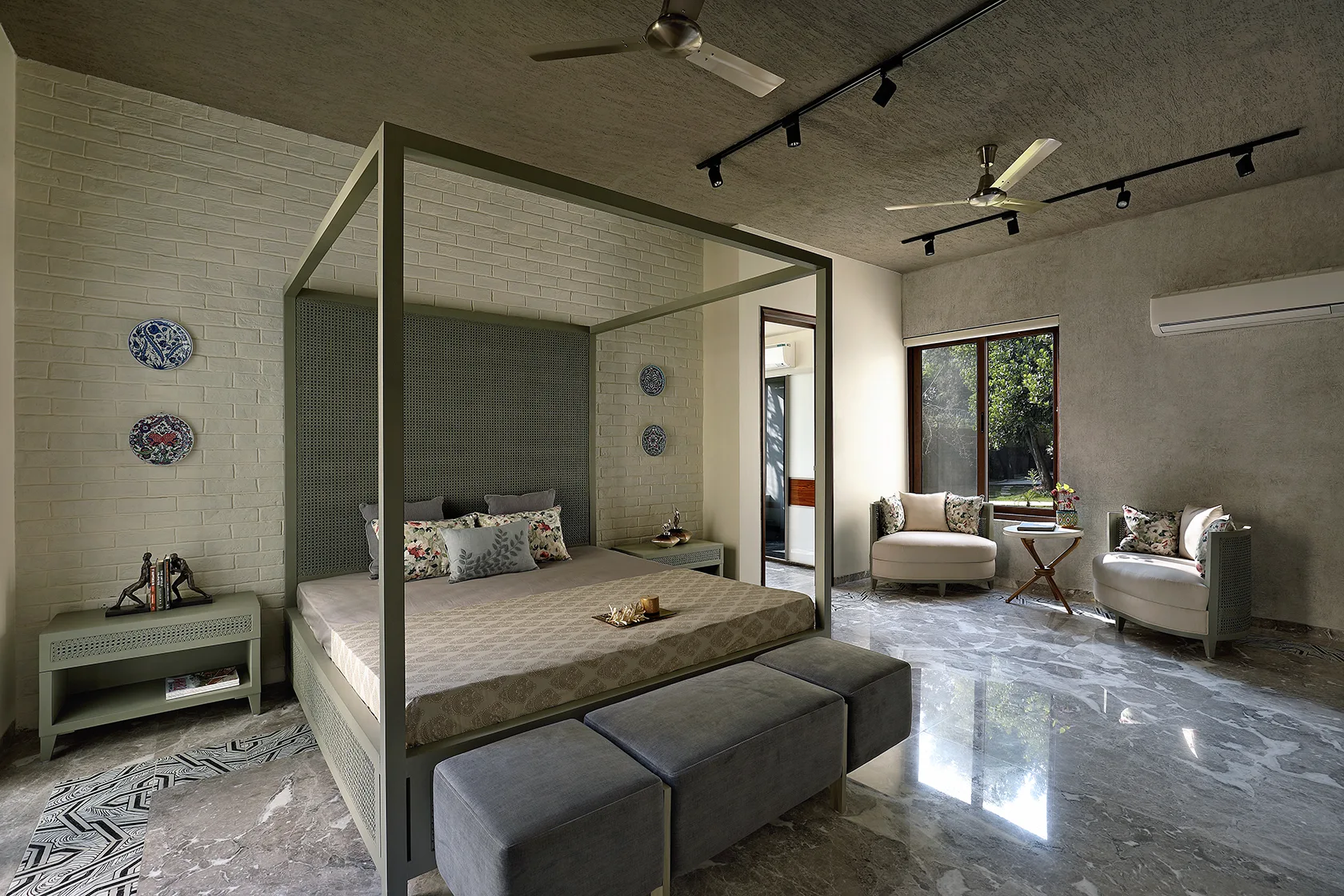 A spacious bedroom features a sage green four-poster canopy bed against a white brick wall with polished marble flooring.