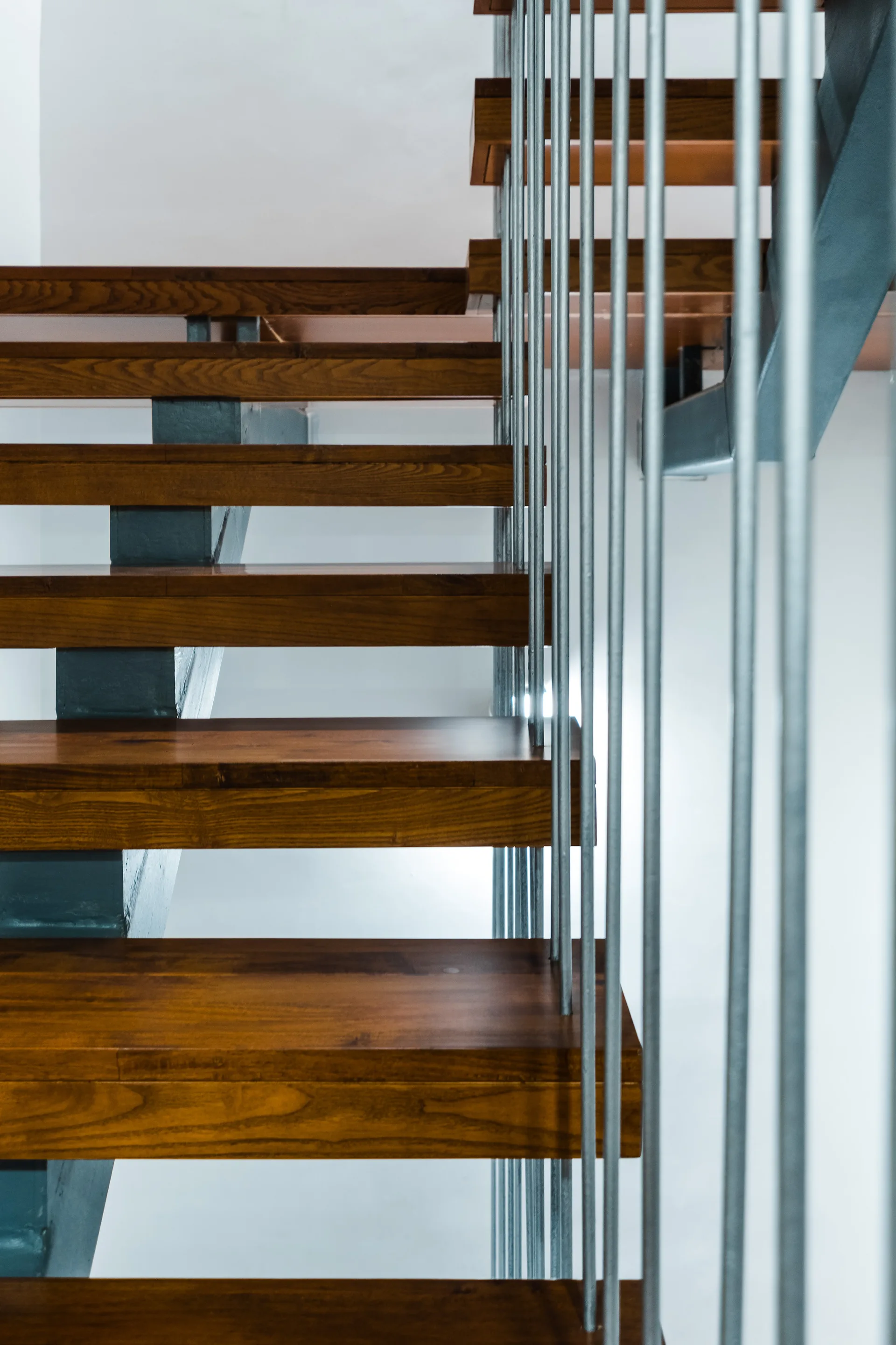 A modern staircase featuring open-riser stained wood treads supported by a dark metal frame and thin vertical metal railing rods.