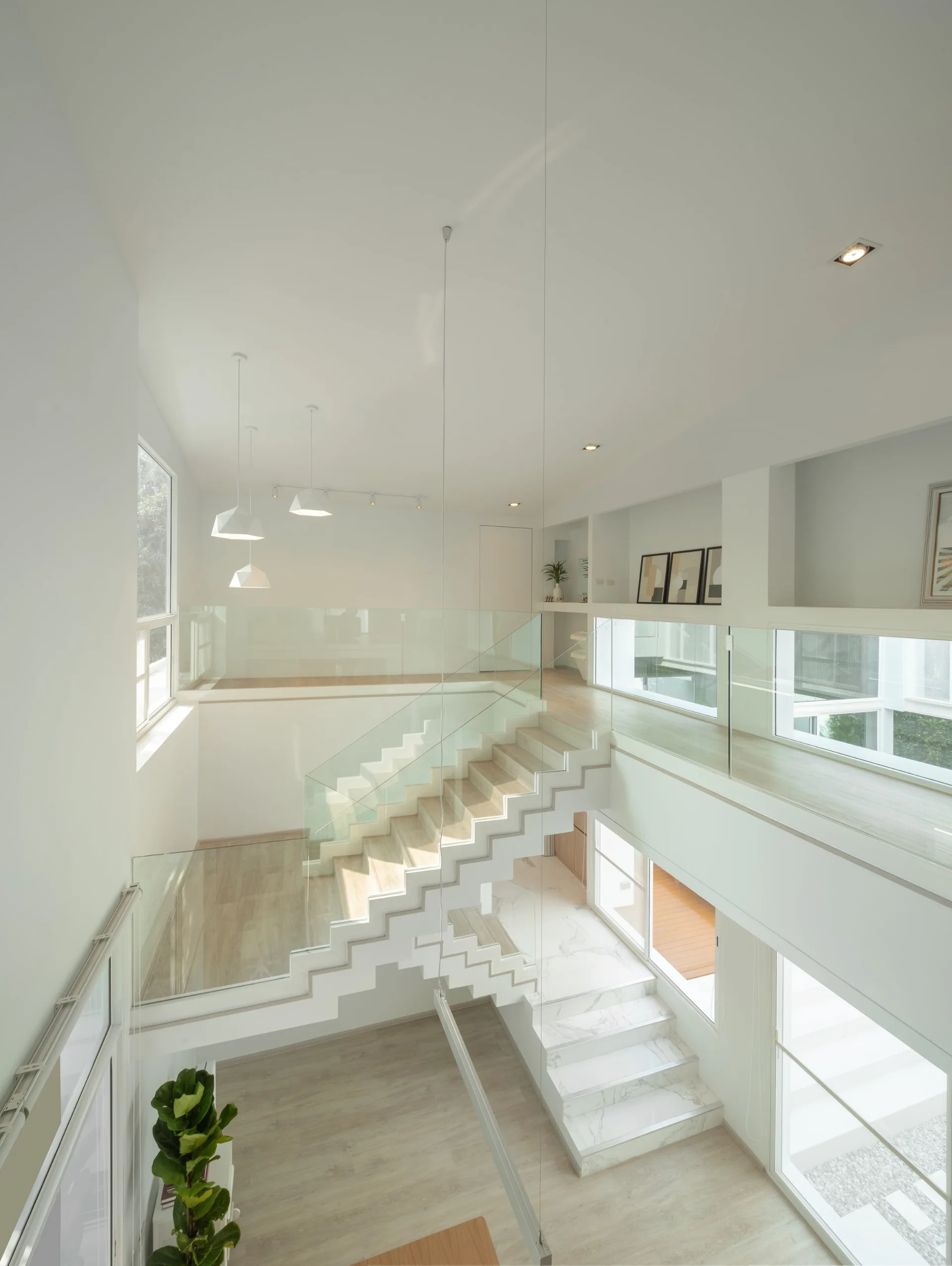 A multi-level minimalist interior featuring a light wood floating staircase with glass railings, white walls, and large windows.