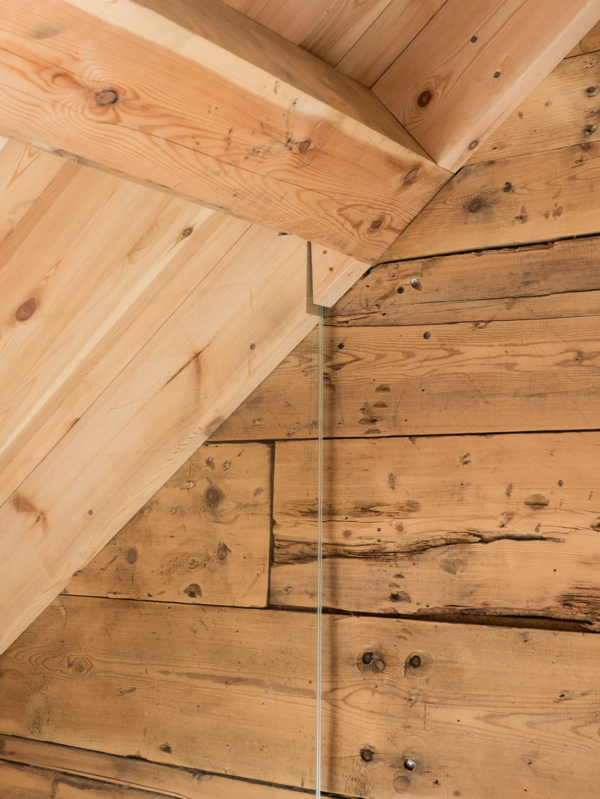 A close-up view of the joinery between a sloped pine plank ceiling with a heavy timber beam and a rustic horizontal log wall.