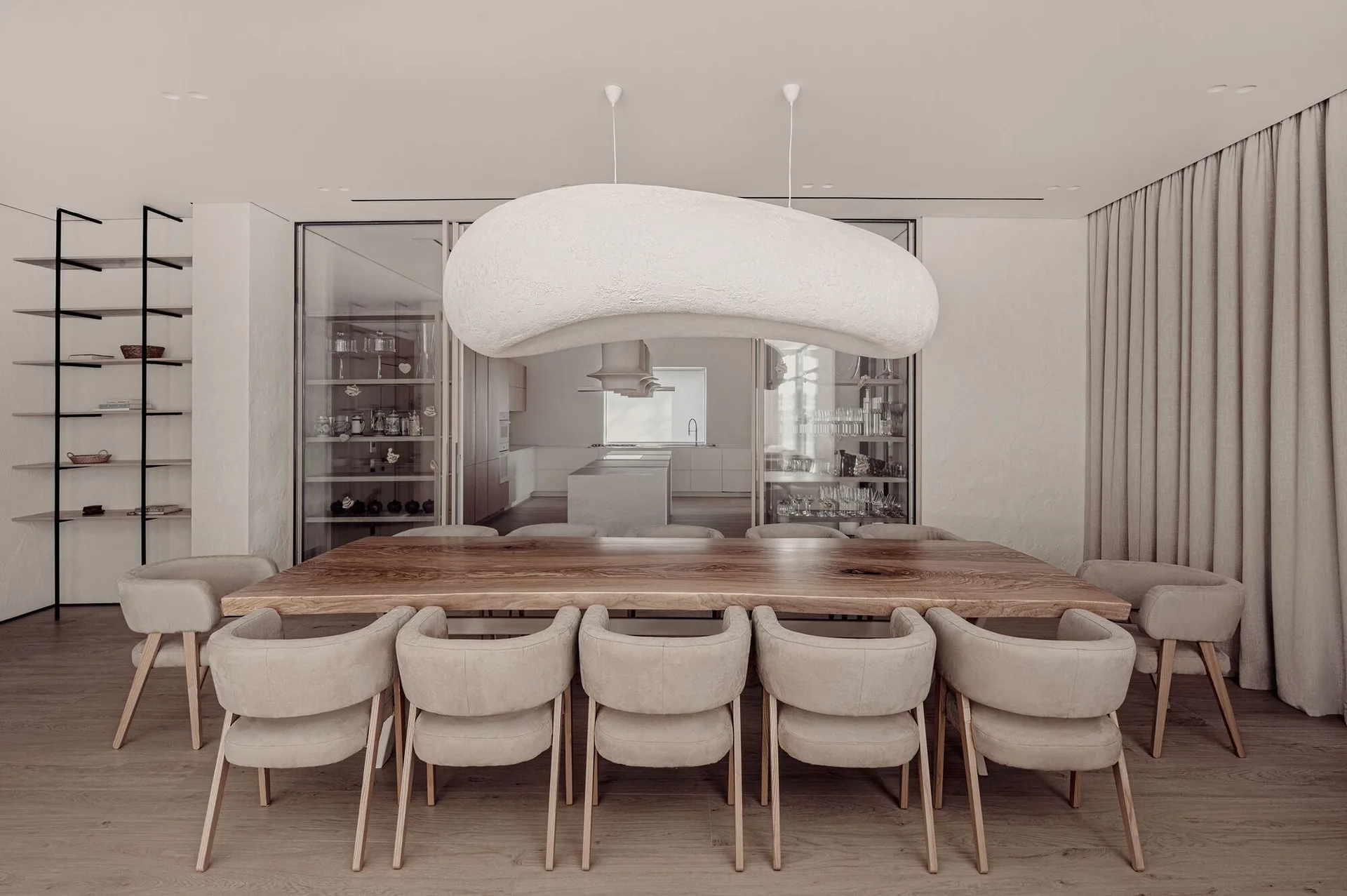 A minimalist dining room featuring a long live-edge wood table, curved upholstered chairs, and a large organic white pendant light.