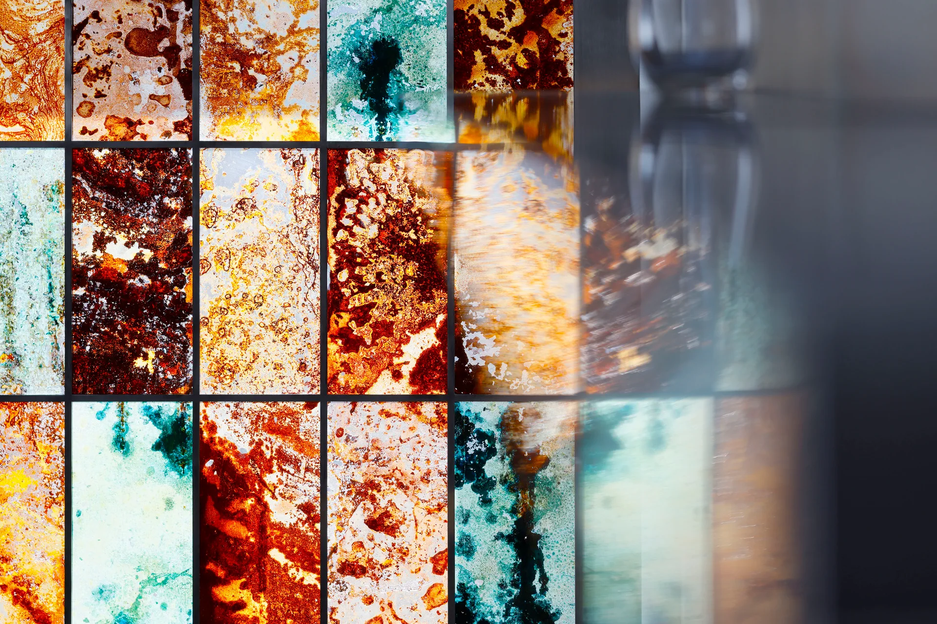 Decorative wall tiles featuring a glossy, oxidized pattern of rust, teal, and copper shades divided by thin dark grid lines.