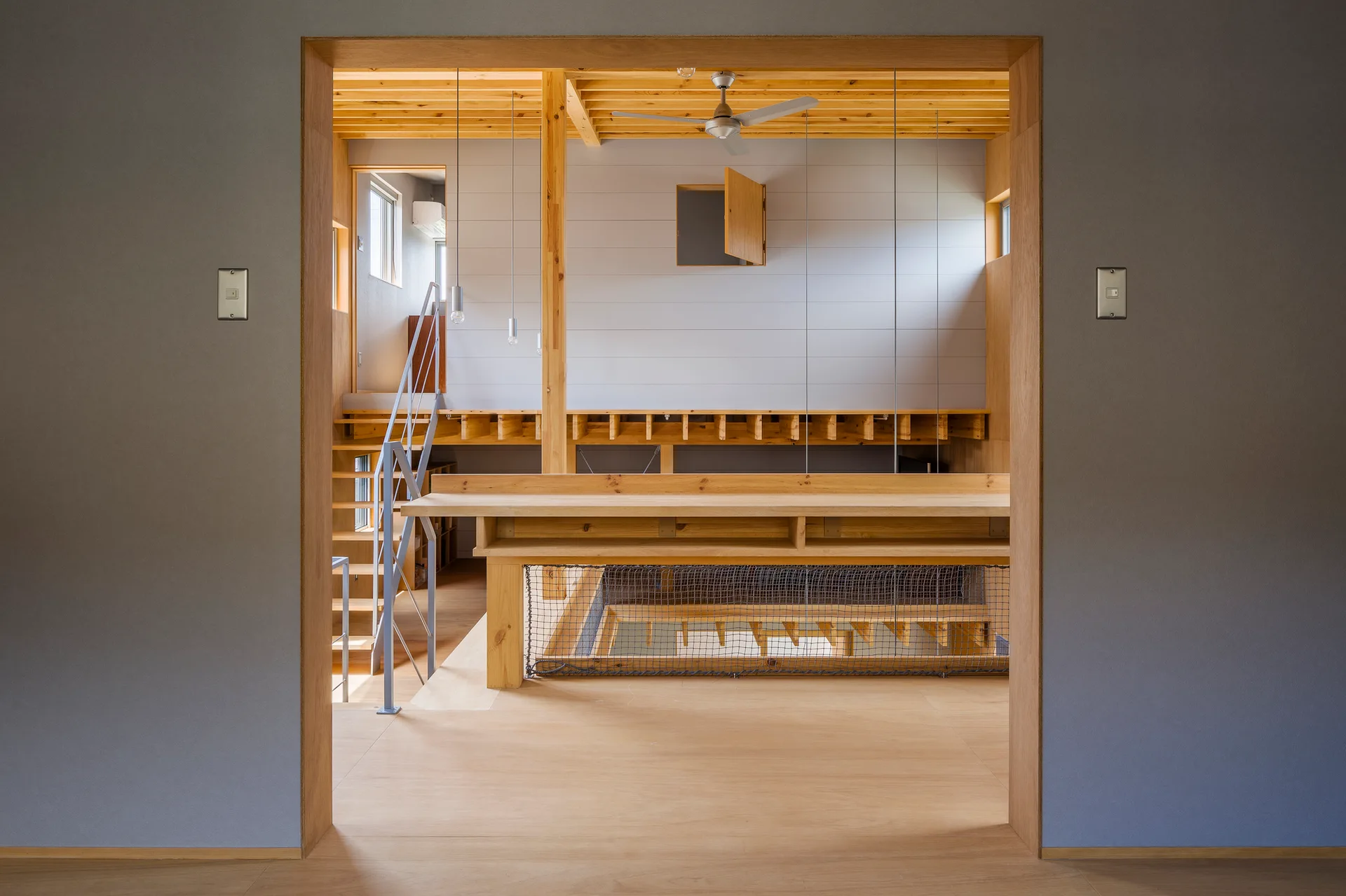 A view through a grey doorway into a modern multi-level wooden home featuring a mezzanine, open staircase, and light wood surfaces.