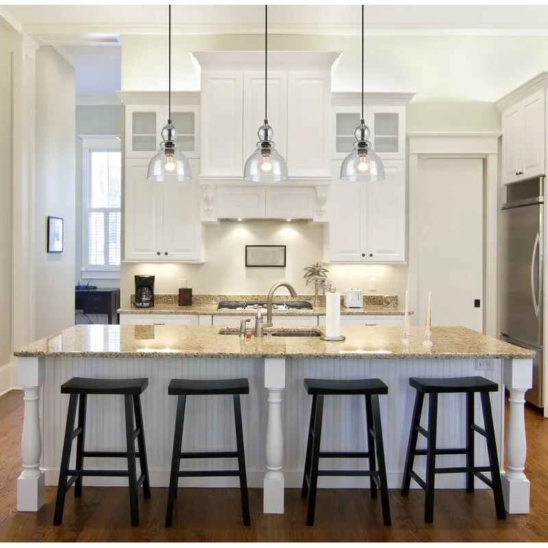 A white kitchen island with a speckled granite countertop, four black backless stools, and three glass pendant lights hanging above.