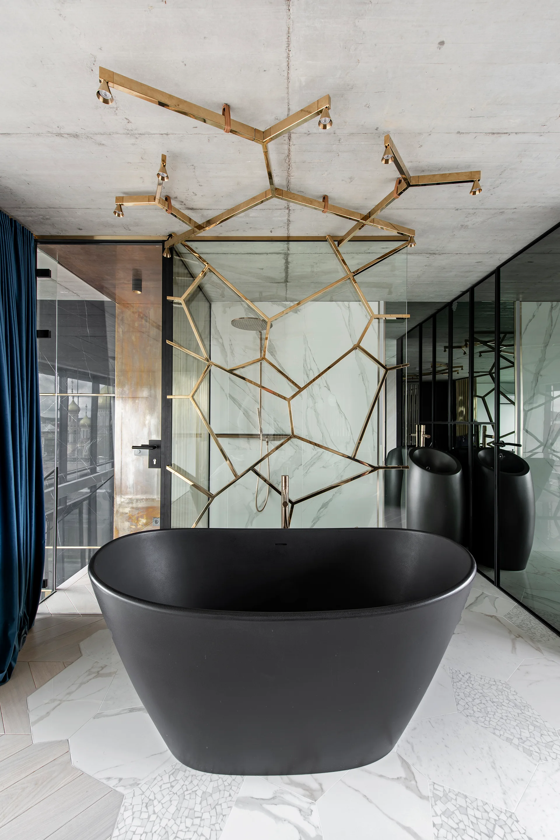 A modern bathroom featuring a matte black freestanding bathtub on white marble hexagonal tiles, with a geometric brass fixture on the ceiling.