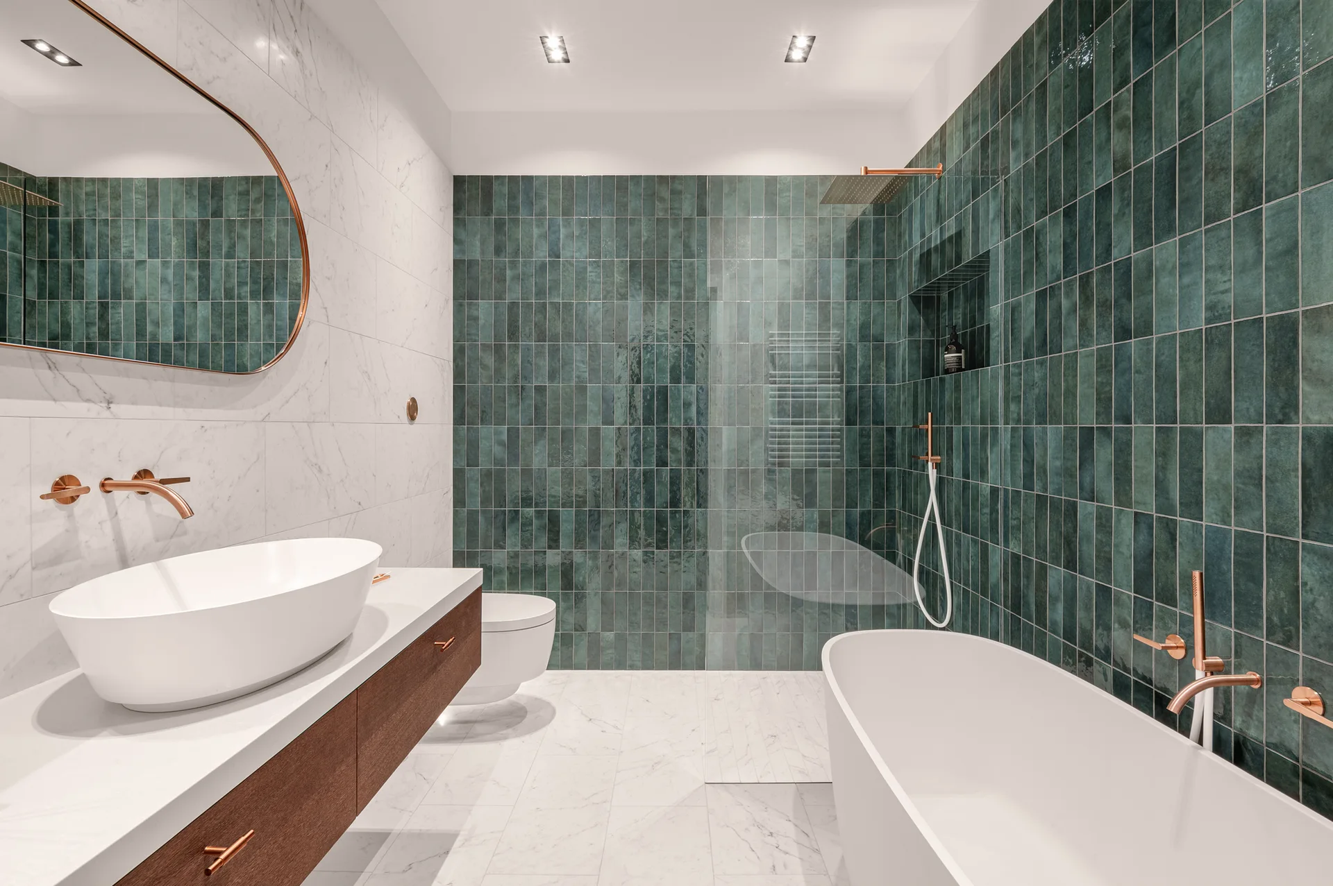A modern bathroom featuring a white freestanding bathtub, a floating wooden vanity with a vessel sink, and vertical teal wall tiles.