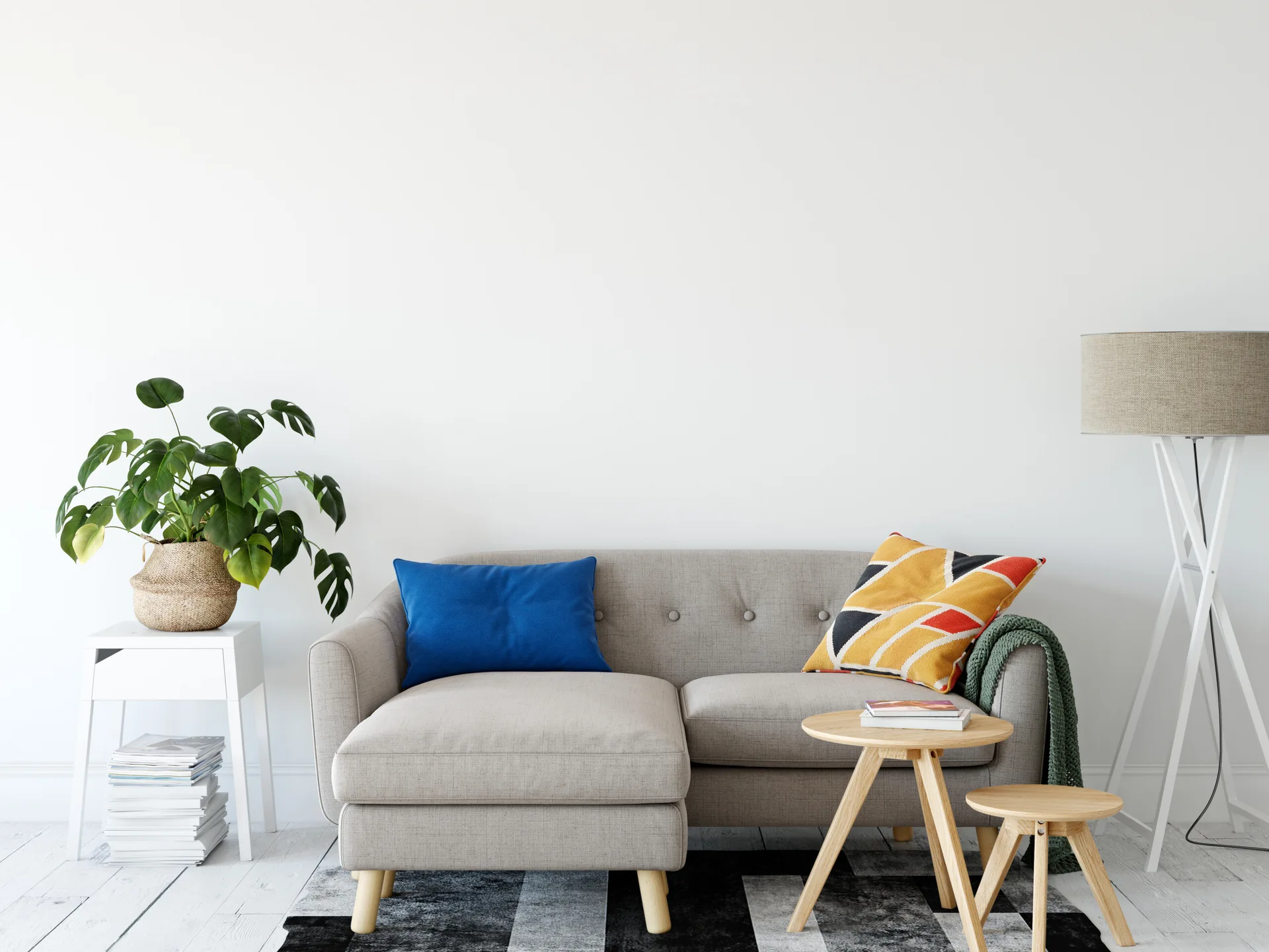 A grey tufted sofa stands on a black and white striped rug in a white-walled living room with nesting tables, a potted plant, and a tripod floor lamp.