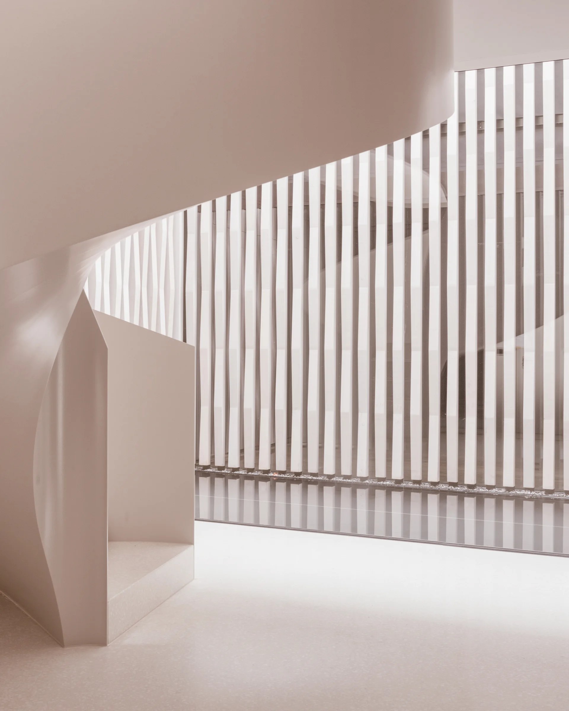 A minimalist beige staircase with a smooth curved design and a built-in house-shaped alcove next to a large window with vertical slats.