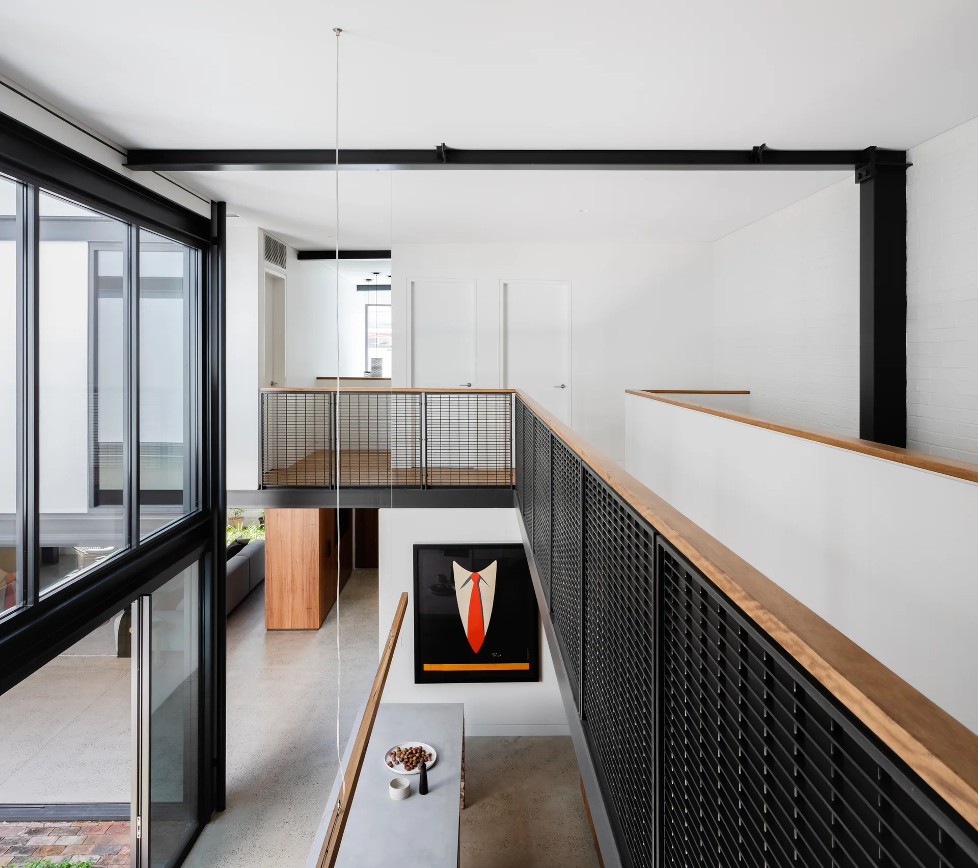 An elevated residential mezzanine features black steel grid railings with wooden handrails overlooking a lower living level with concrete floors.