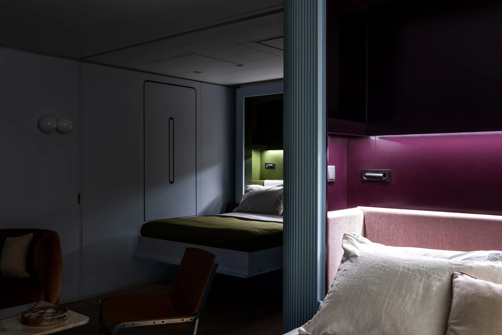 A modern bedroom featuring two recessed sleeping areas with colorful magenta and green backdrops divided by a fluted light blue column.