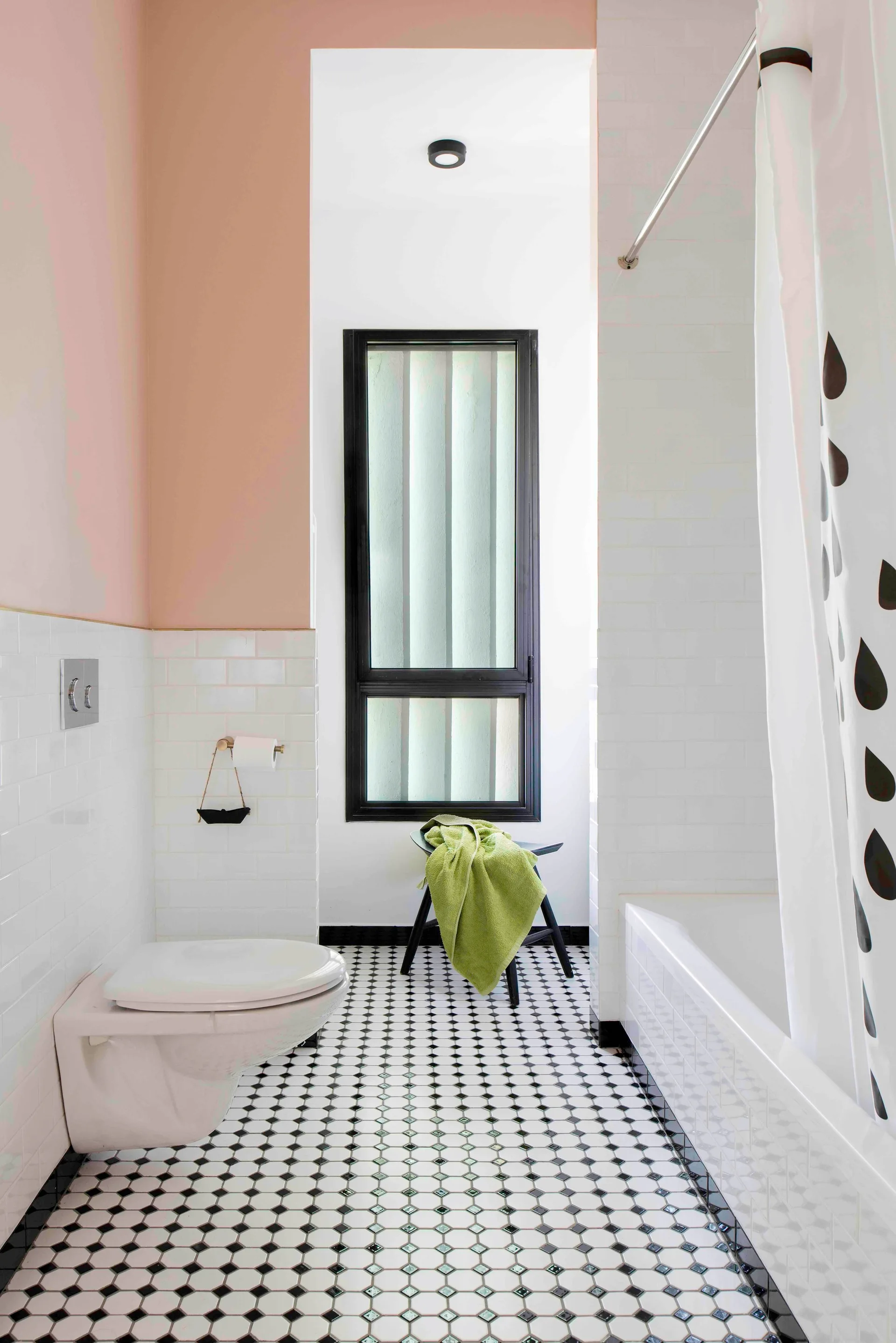 A modern bathroom features a black and white mosaic tile floor, white subway tiles on the walls, and a wall-mounted toilet near a bathtub.