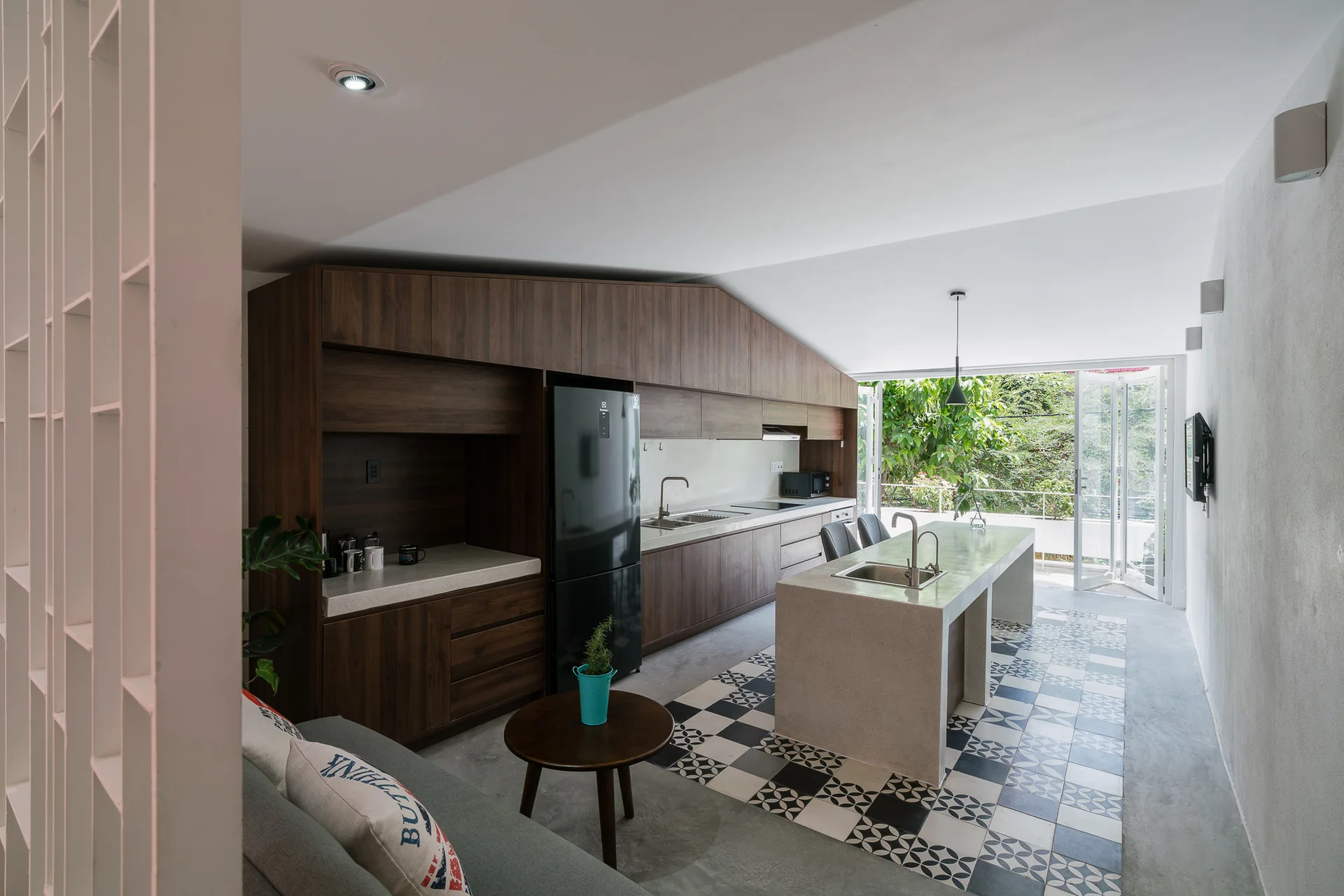 A modern kitchen featuring dark wood cabinetry, a concrete island, and a black and white patterned tile inlay on the floor.