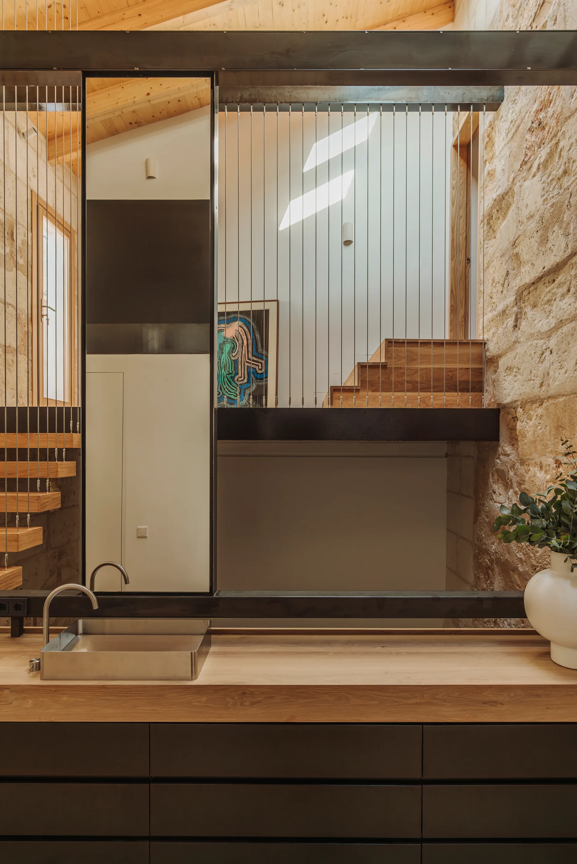 A modern wood vanity with a stainless steel sink stands near an open staircase featuring floating wood treads and vertical cable railings.