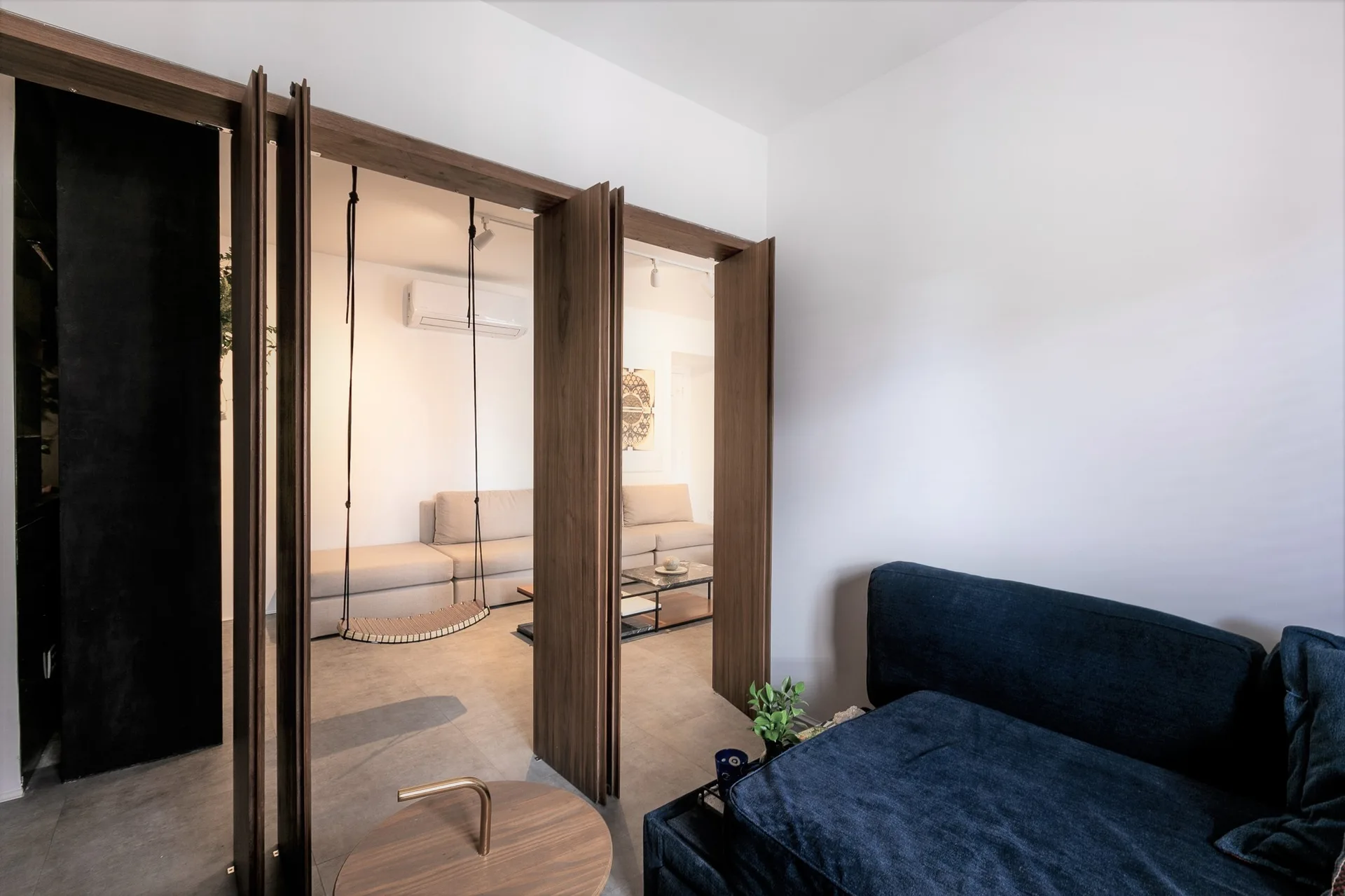 A dark blue sofa sits in a room separated from a beige lounge area by a wooden folding partition with a hanging swing chair.
