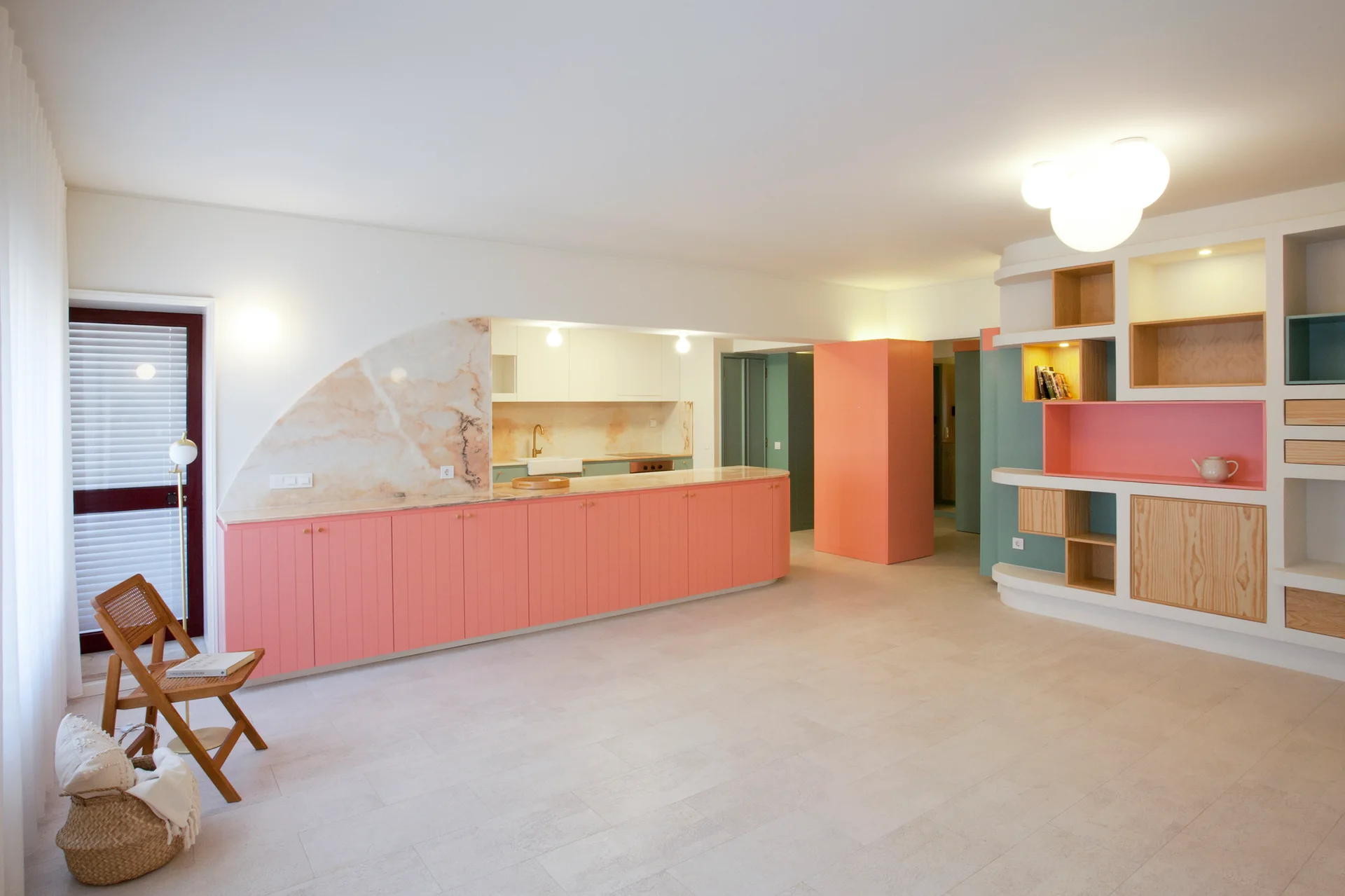 An open kitchen and living space features a long row of coral cabinets, a curved marble backsplash, and a large custom modular shelving unit.