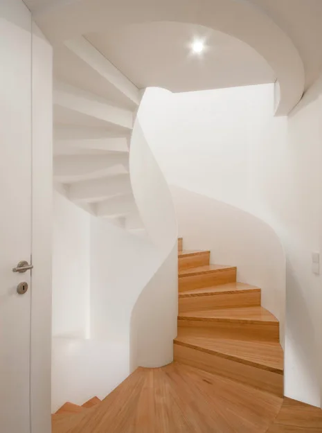 A minimalist white spiral staircase with warm natural wood treads and a continuous curved solid plaster railing.