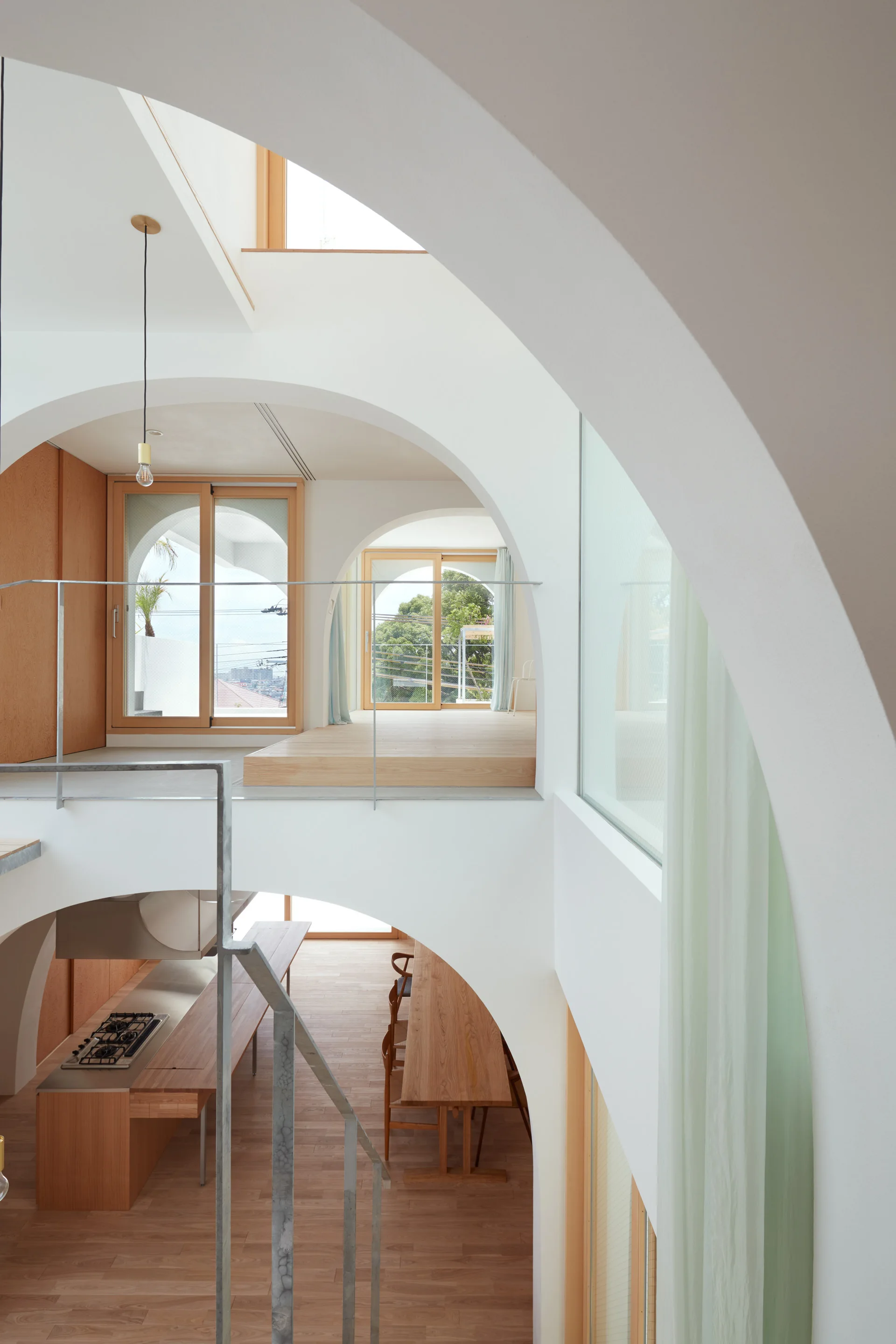 A multi-level minimalist interior featuring large white plaster archways, light wood flooring, and a dining table seen from above.