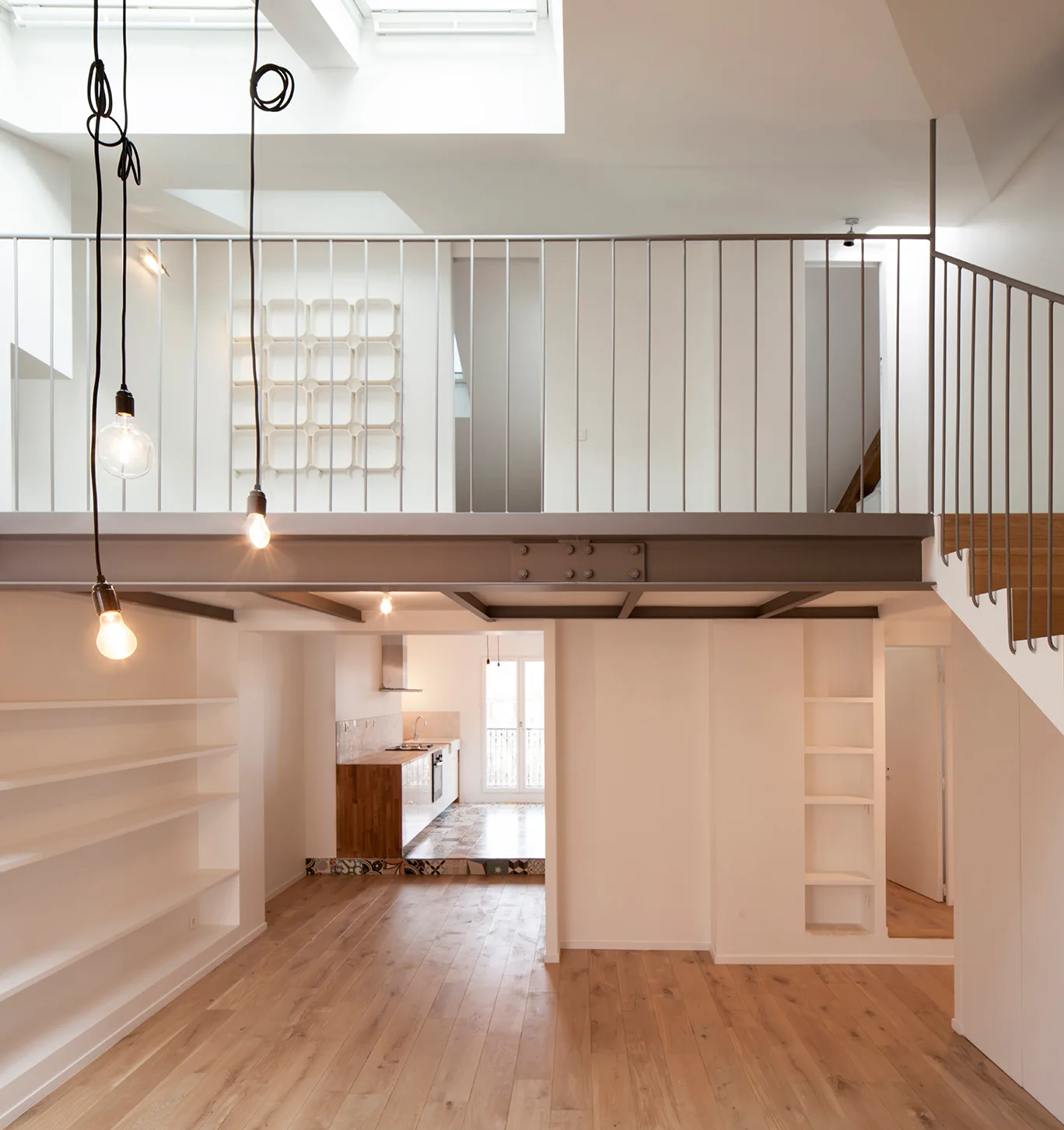 A duplex interior features a white metal mezzanine railing supported by an exposed steel beam, wooden floors, and hanging pendant bulbs.