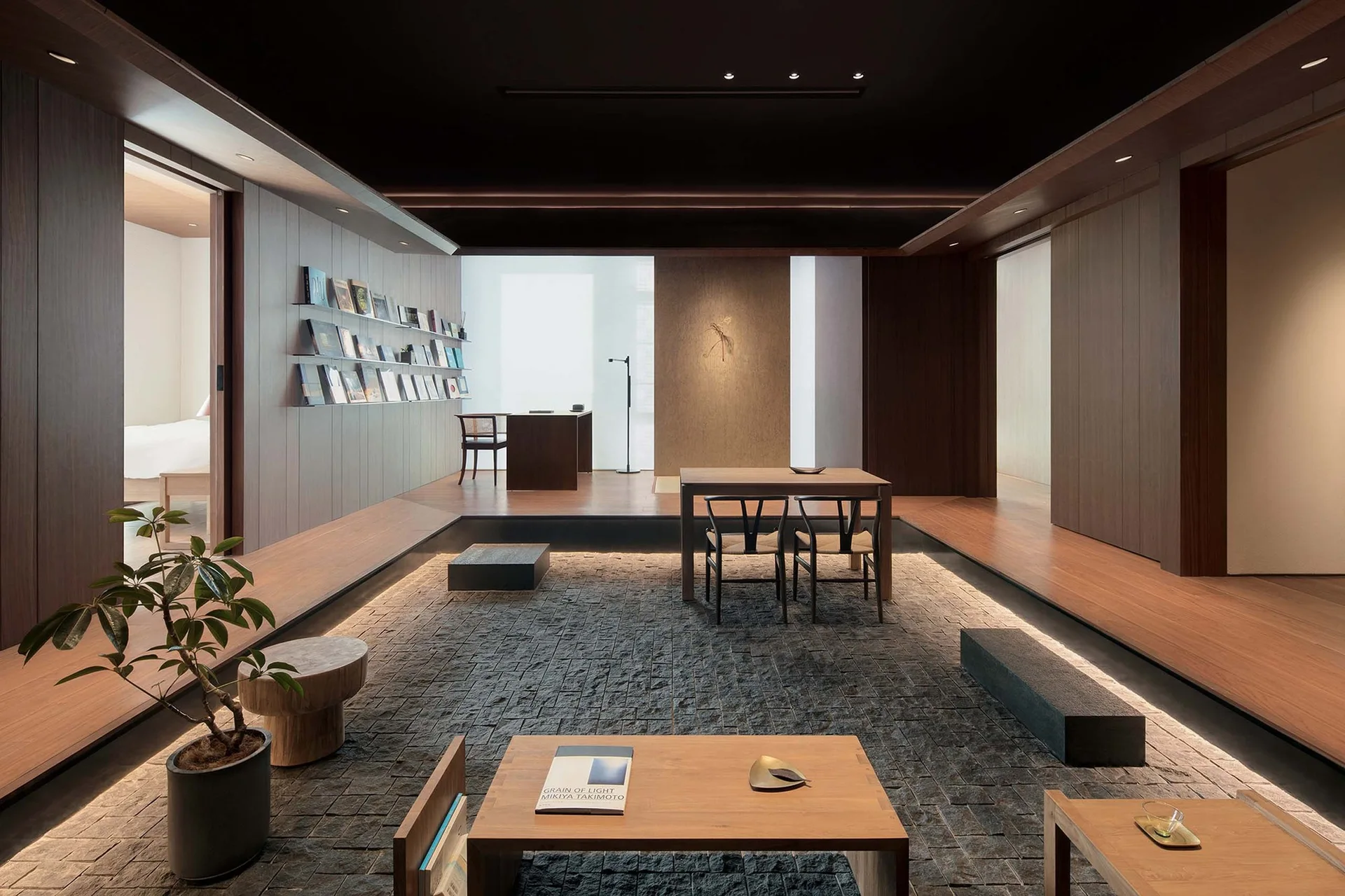 A minimalist living room features a sunken dark stone floor surrounded by a raised wooden platform with integrated glowing cove lighting.