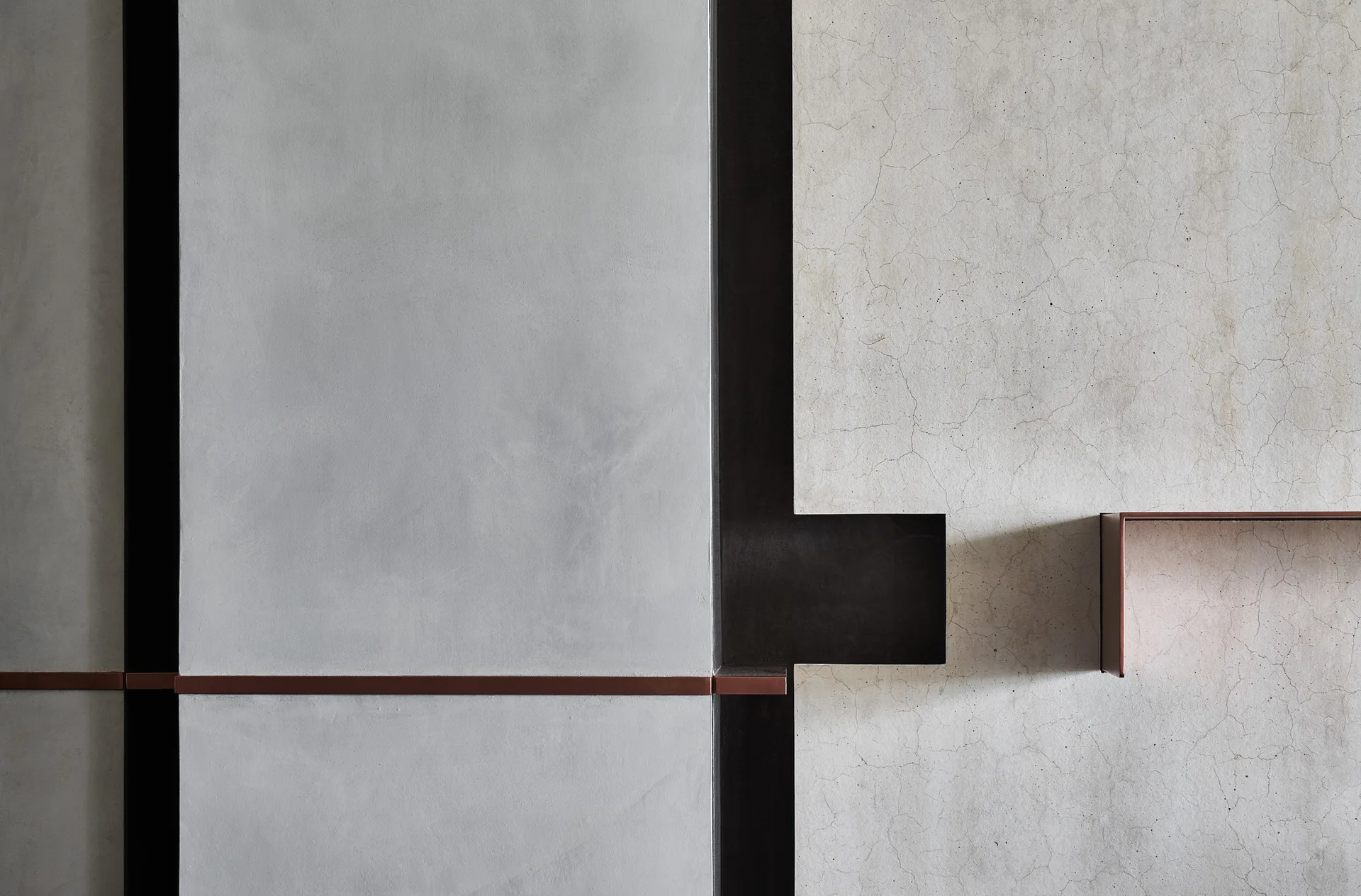 A close-up of a minimalist wall showing smooth gray plaster and cracked white plaster panels divided by dark metal lines.