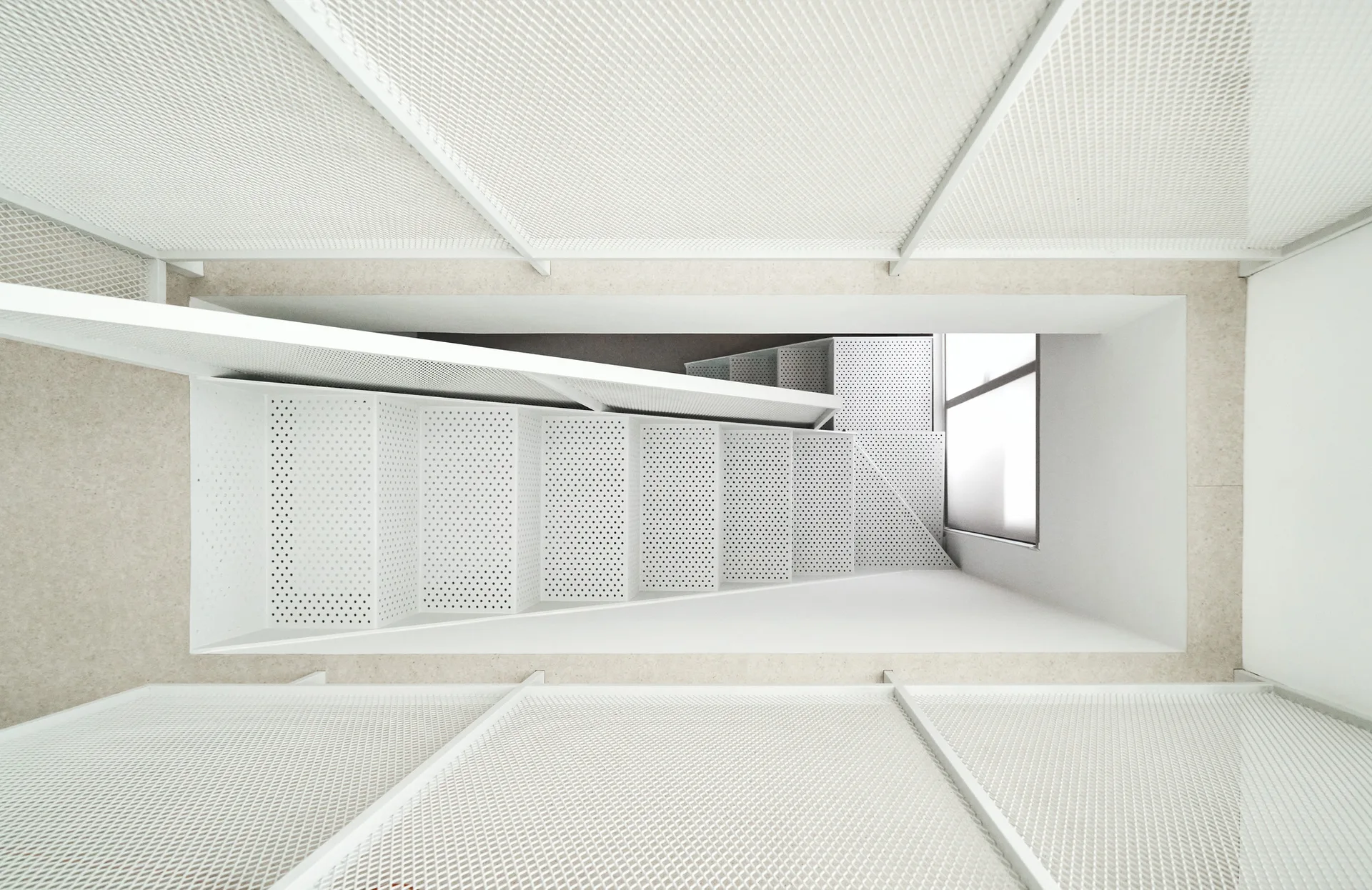 Looking down a minimalist white stairwell featuring perforated metal steps and mesh safety screens.