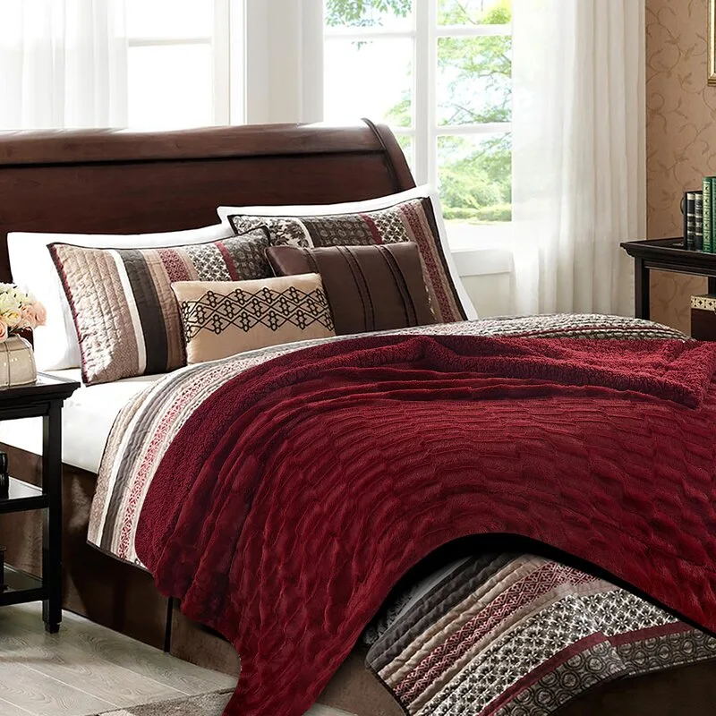 A dark wood bed dressed in a textured burgundy quilt and patterned accent pillows sits in front of a bright window.