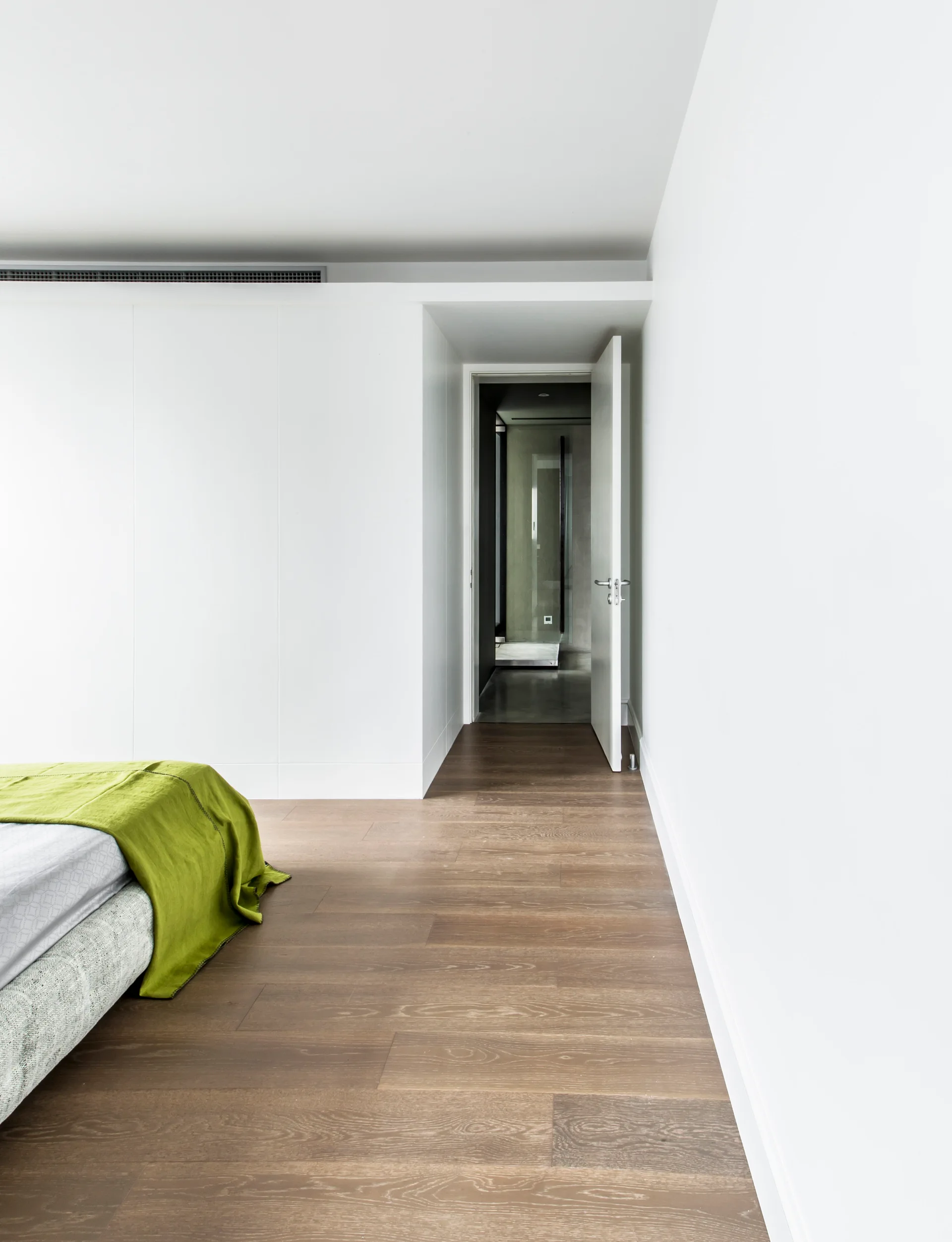 A minimalist white bedroom featuring seamless built-in closets, hardwood flooring, and a bed corner with a green throw blanket.
