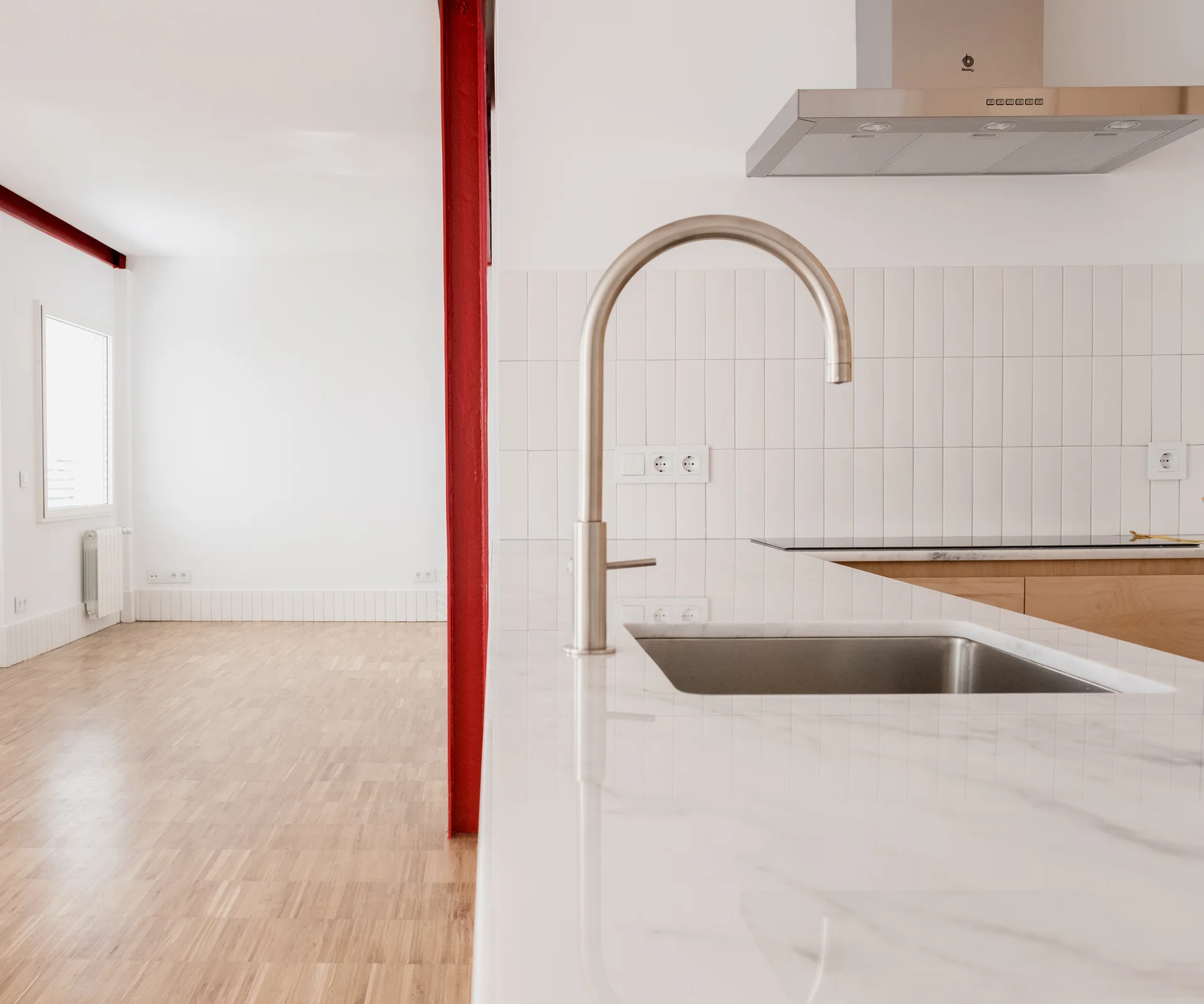 A modern kitchen island with a white marble countertop and stainless steel faucet stands next to a bright red steel I-beam.