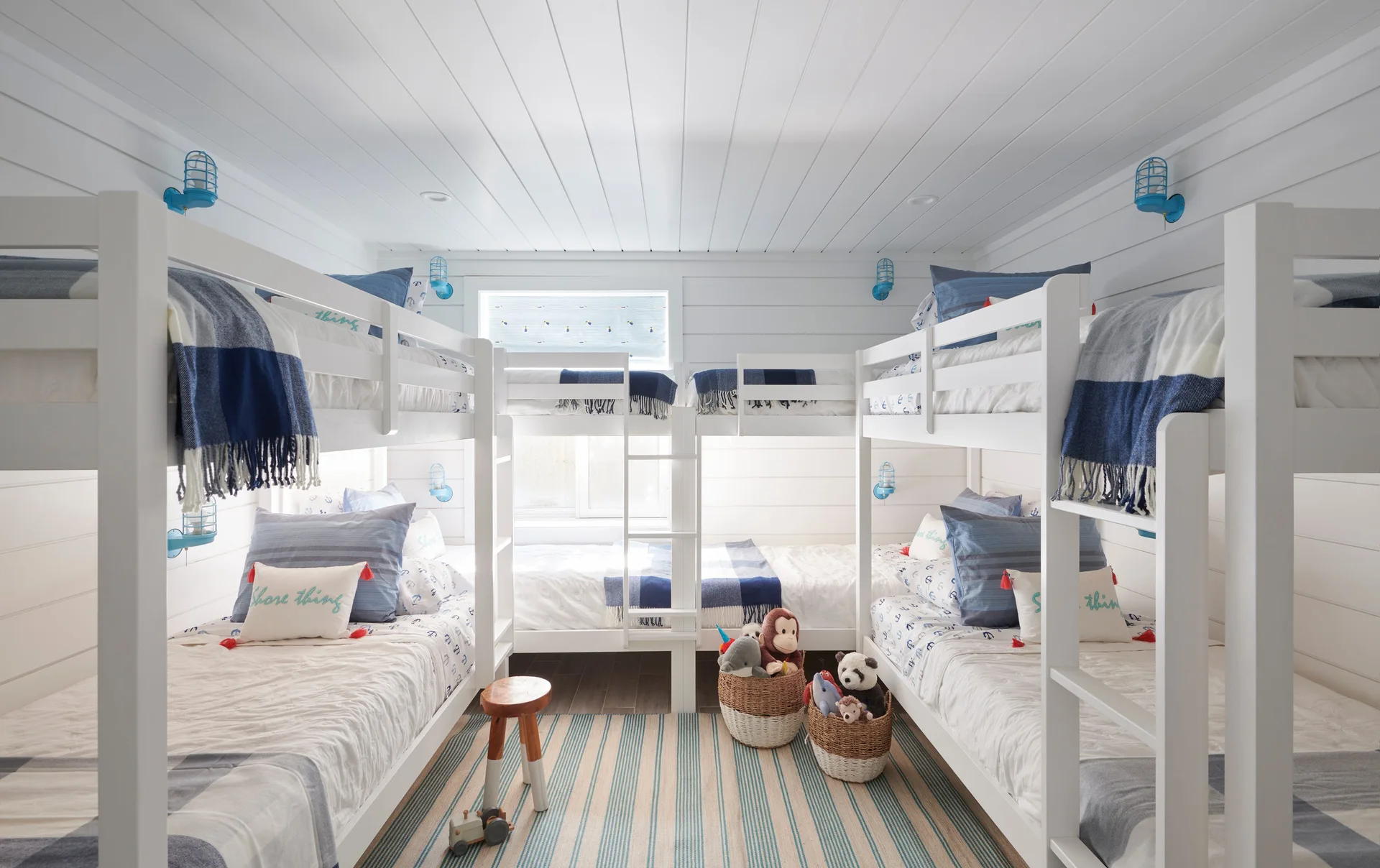 A shared children's bedroom featuring white wooden bunk beds arranged symmetrically along shiplap walls with blue caged wall sconces.