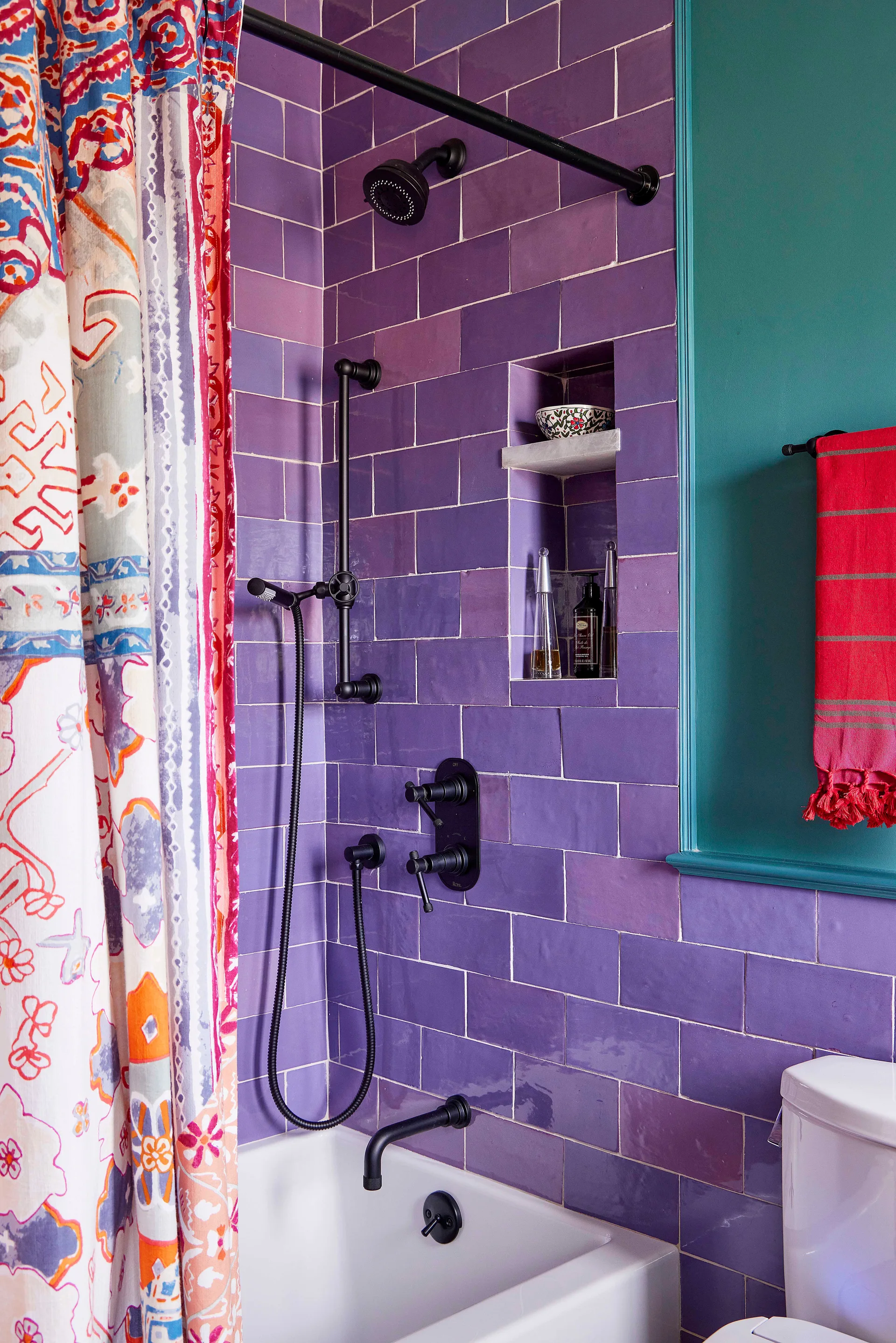 A bathroom featuring purple subway tile walls, a white bathtub, matte black shower fixtures, a colorful patterned curtain, and a recessed niche shelf.