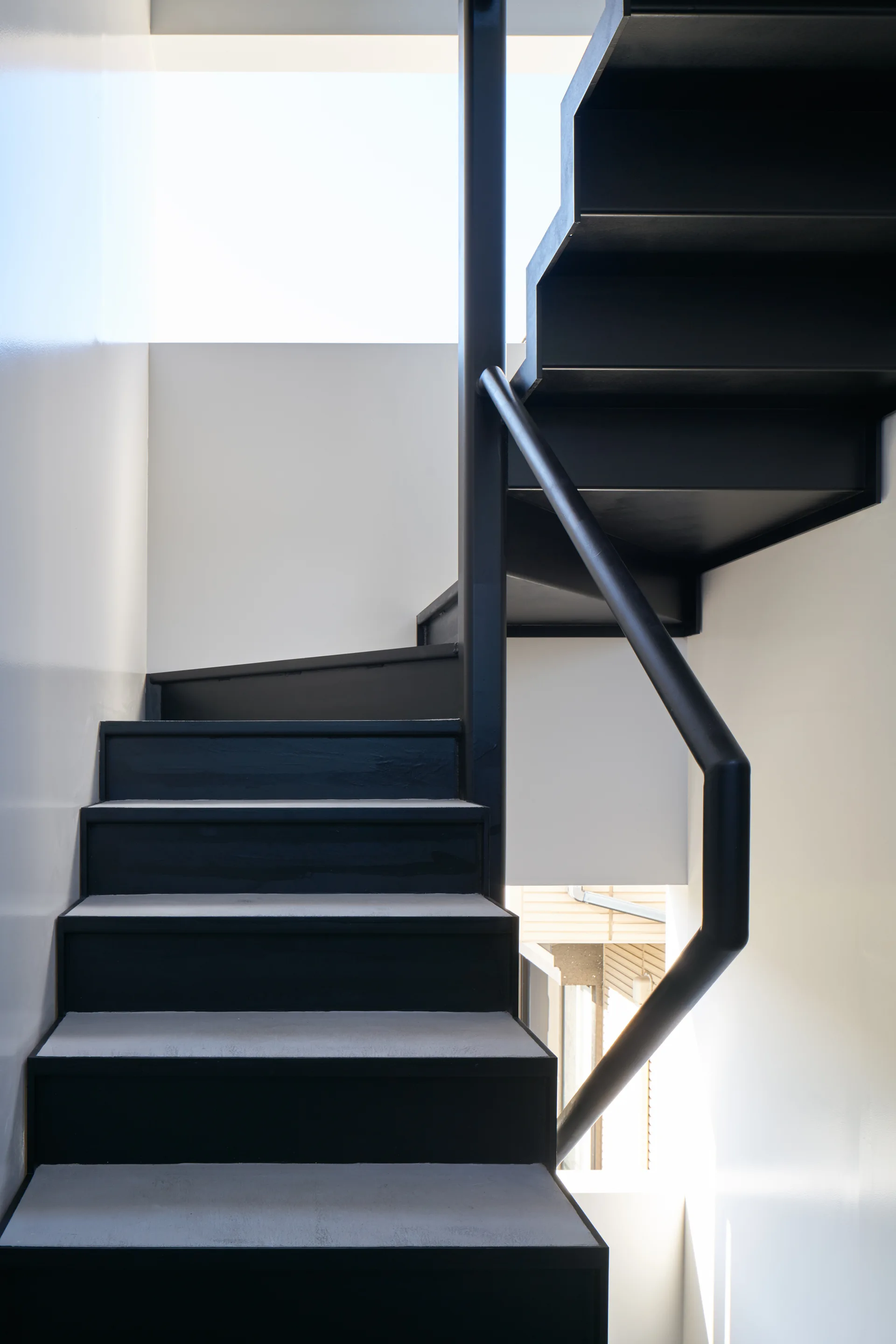 A minimalist black metal staircase with a simple tubular handrail ascends between clean white walls.
